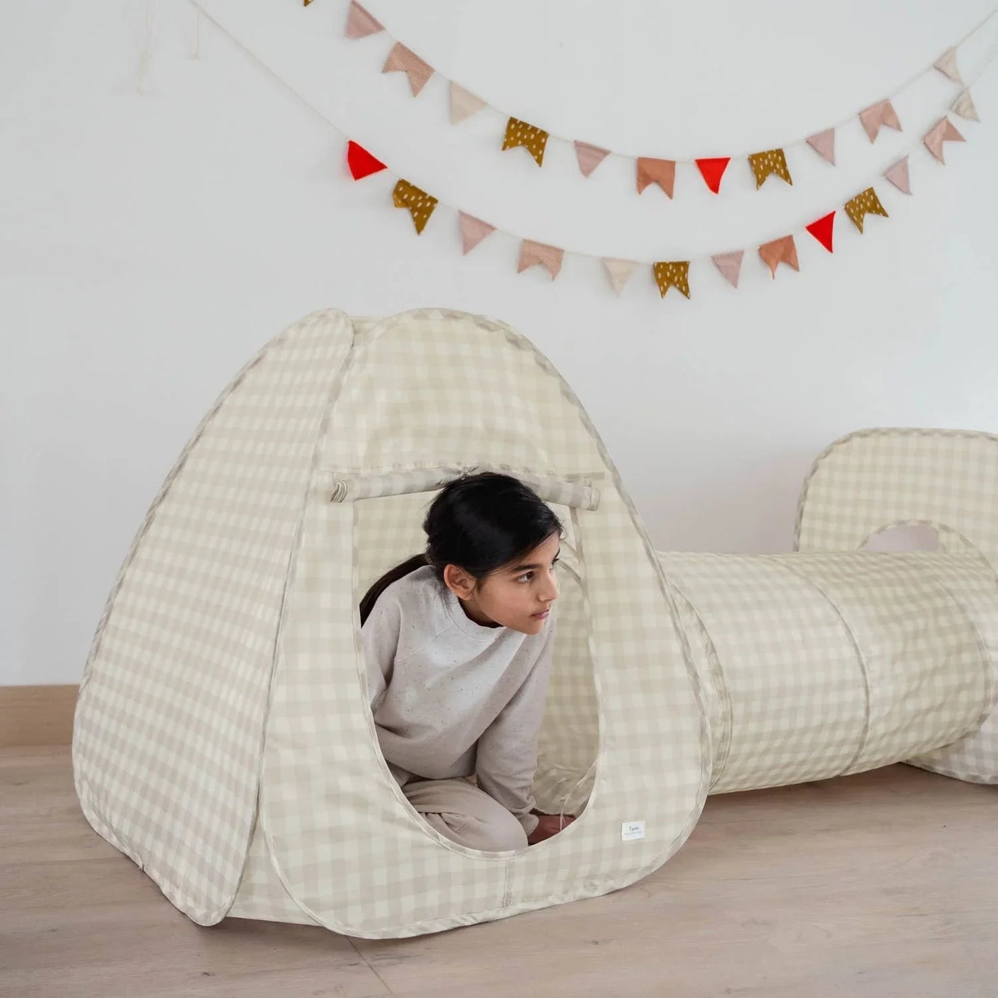 Child playing inside beige checkered indoor play tent and tunnel with decorative flags, Come see us at Awaken, Franklin, Tennessee