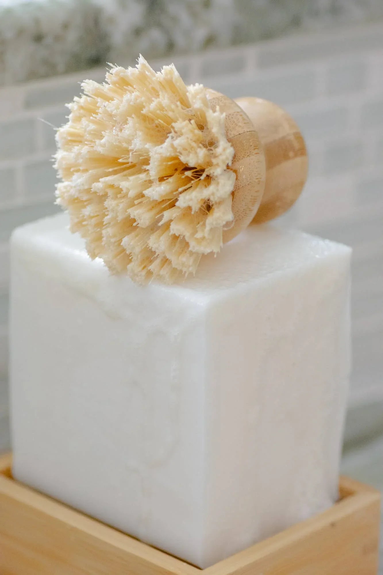 Natural bristle brush on large white soap block with wooden tray, bathroom setting. Come see us at Awaken, Franklin, Tennessee