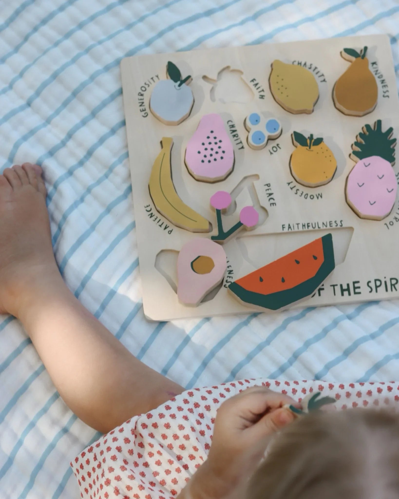 Child playing with wooden fruit puzzle on striped blanket, educational toy. Come see us at Awaken, Franklin, Tennessee