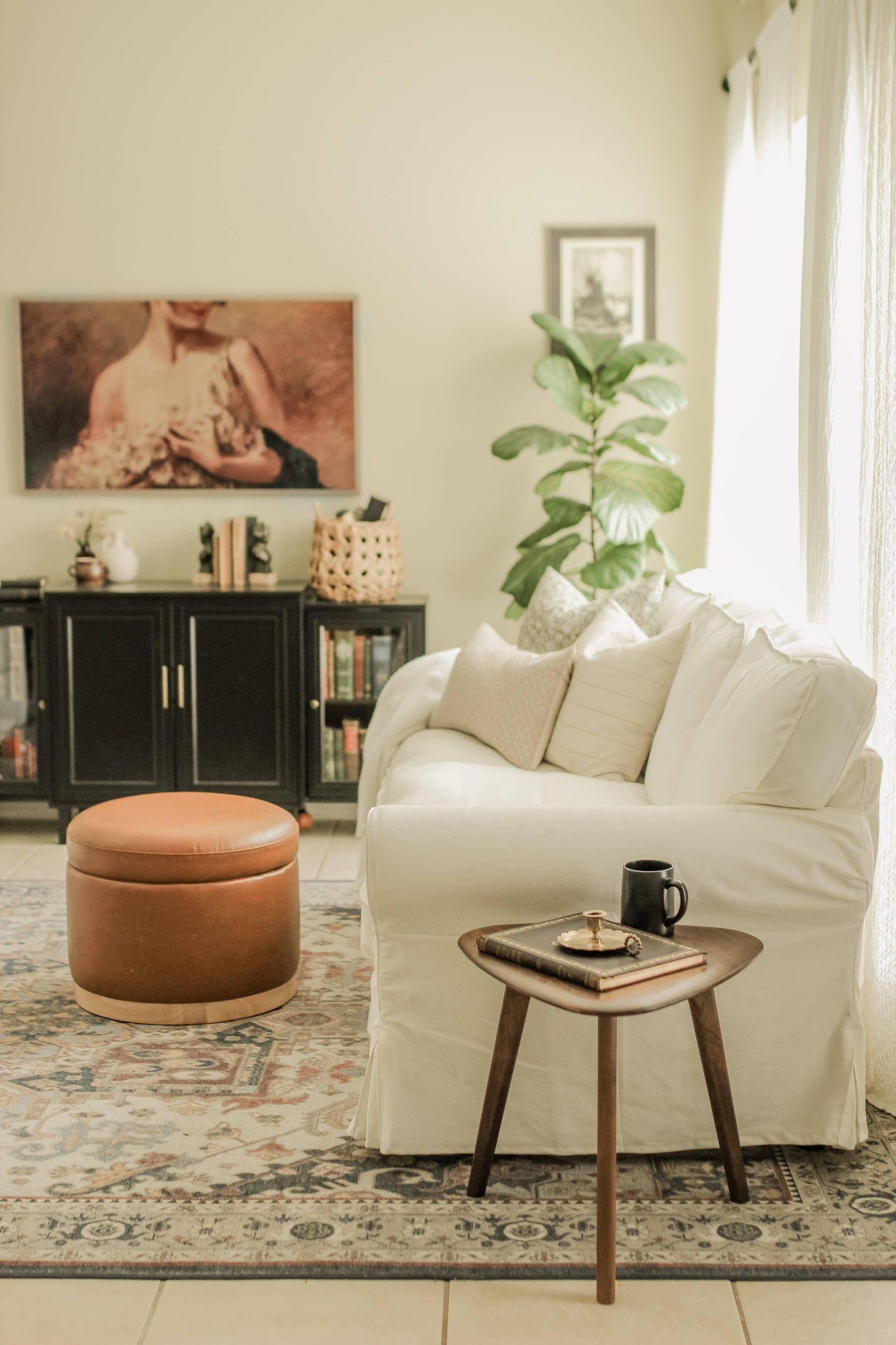 Bright living room with white sofa, brown ottoman, wooden side table, and leafy plant. Come see us at Awaken, Franklin, Tennessee