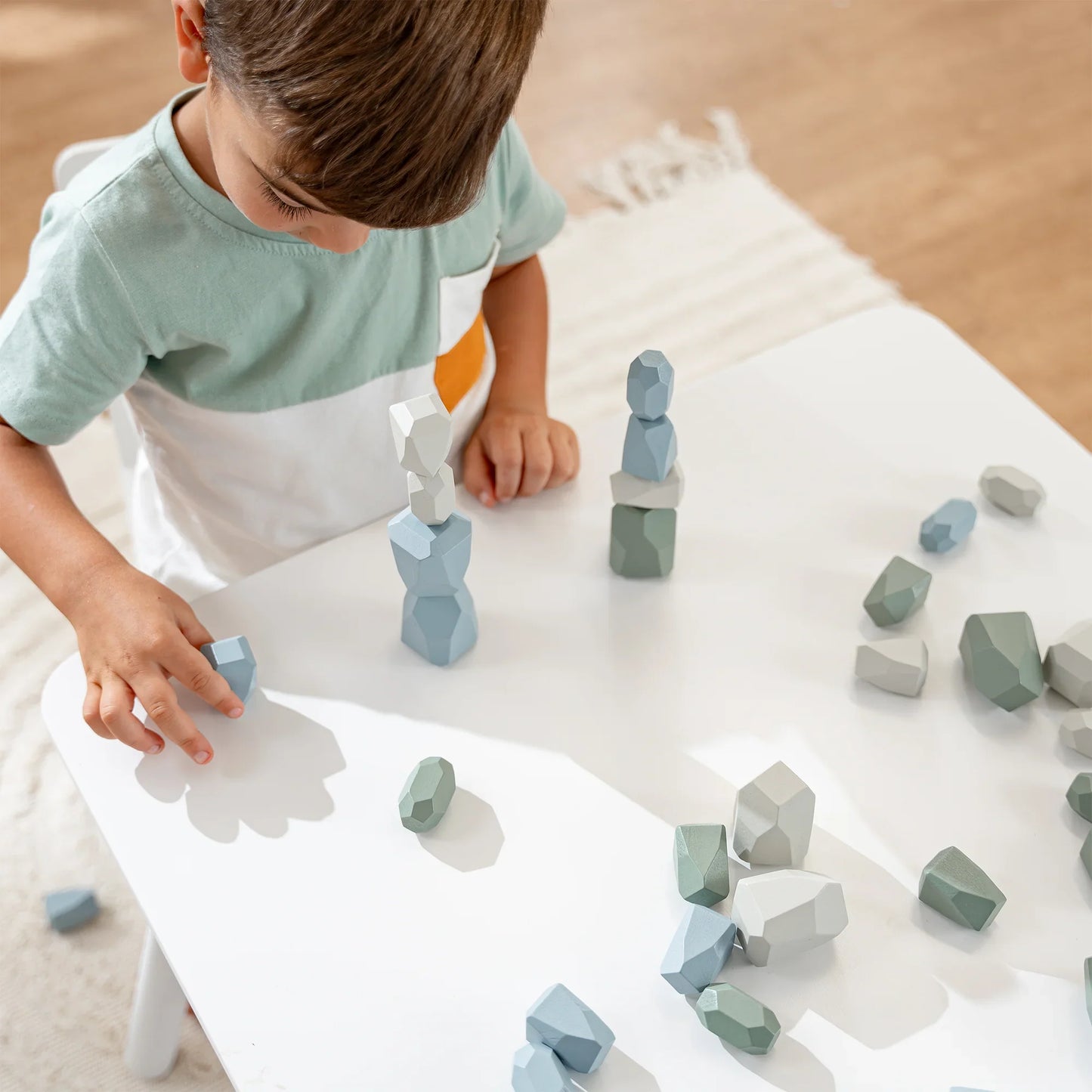 Young boy stacking pastel-colored wooden blocks on a white table, creative playtime, come see us at Awaken, Franklin, Tennessee