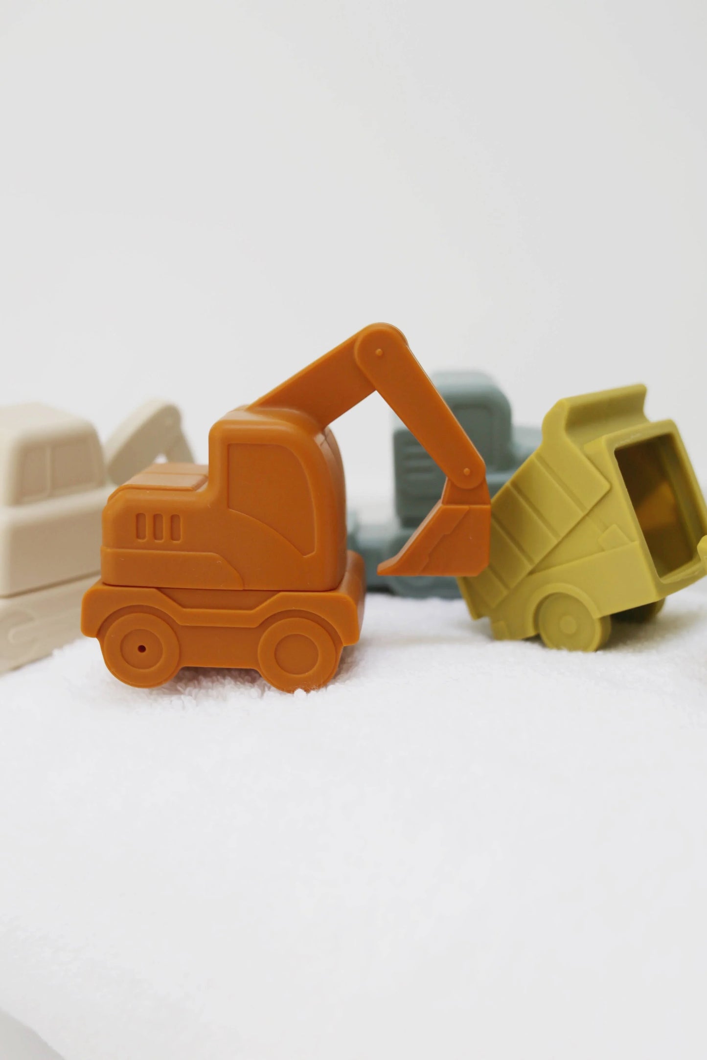 Orange toy excavator with other construction vehicles in soft muted colors on white surface. Come see us at Awaken, Franklin, Tennessee