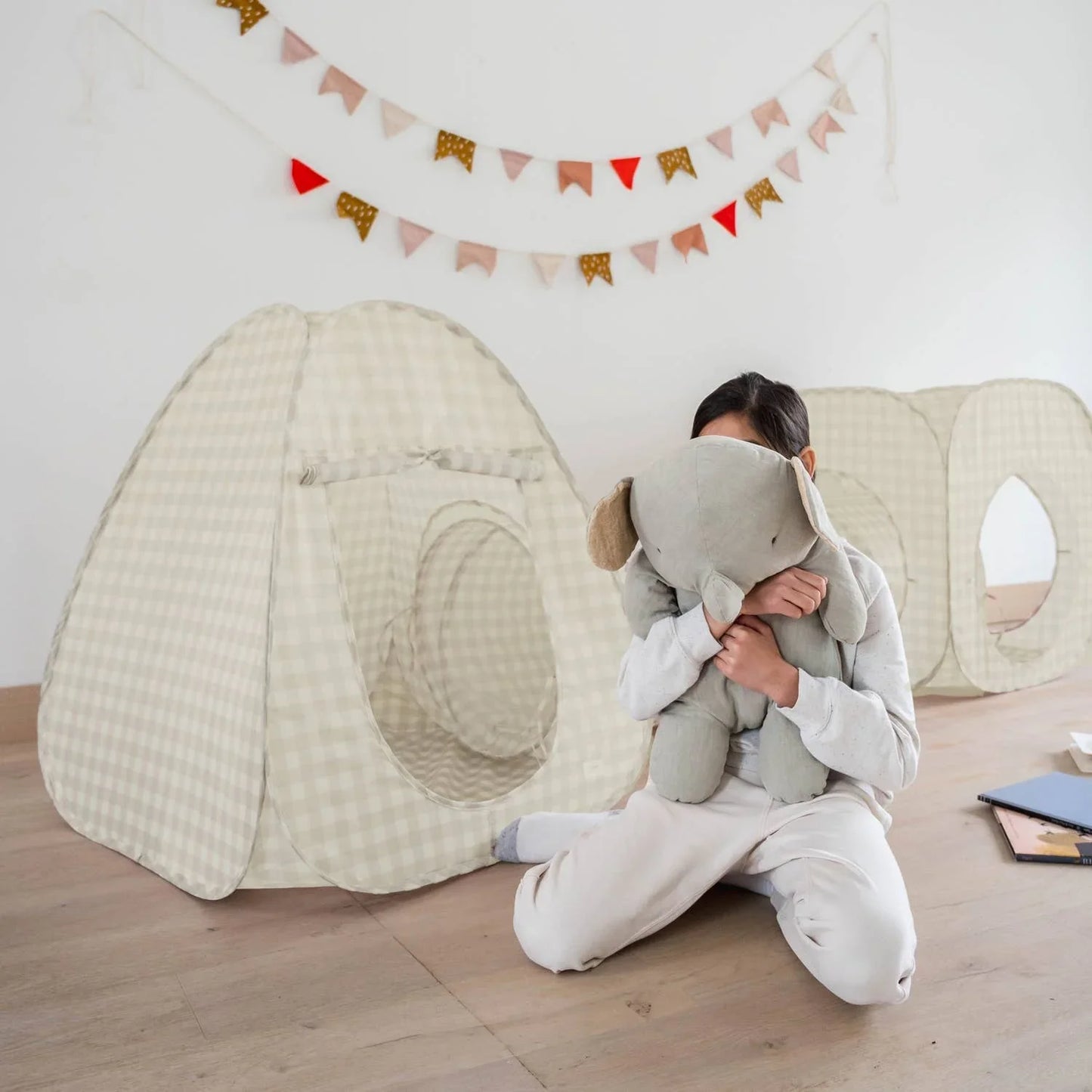 Child hugging a large stuffed elephant in a room with beige checkered play tents and colorful pennant banners. Come see us at Awaken, Franklin, Tennessee