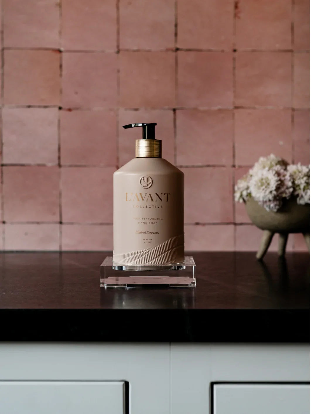 L'AVANT Collective hand soap on dark counter with pink tile and flowers, Come see us at Awaken, Franklin, Tennessee.