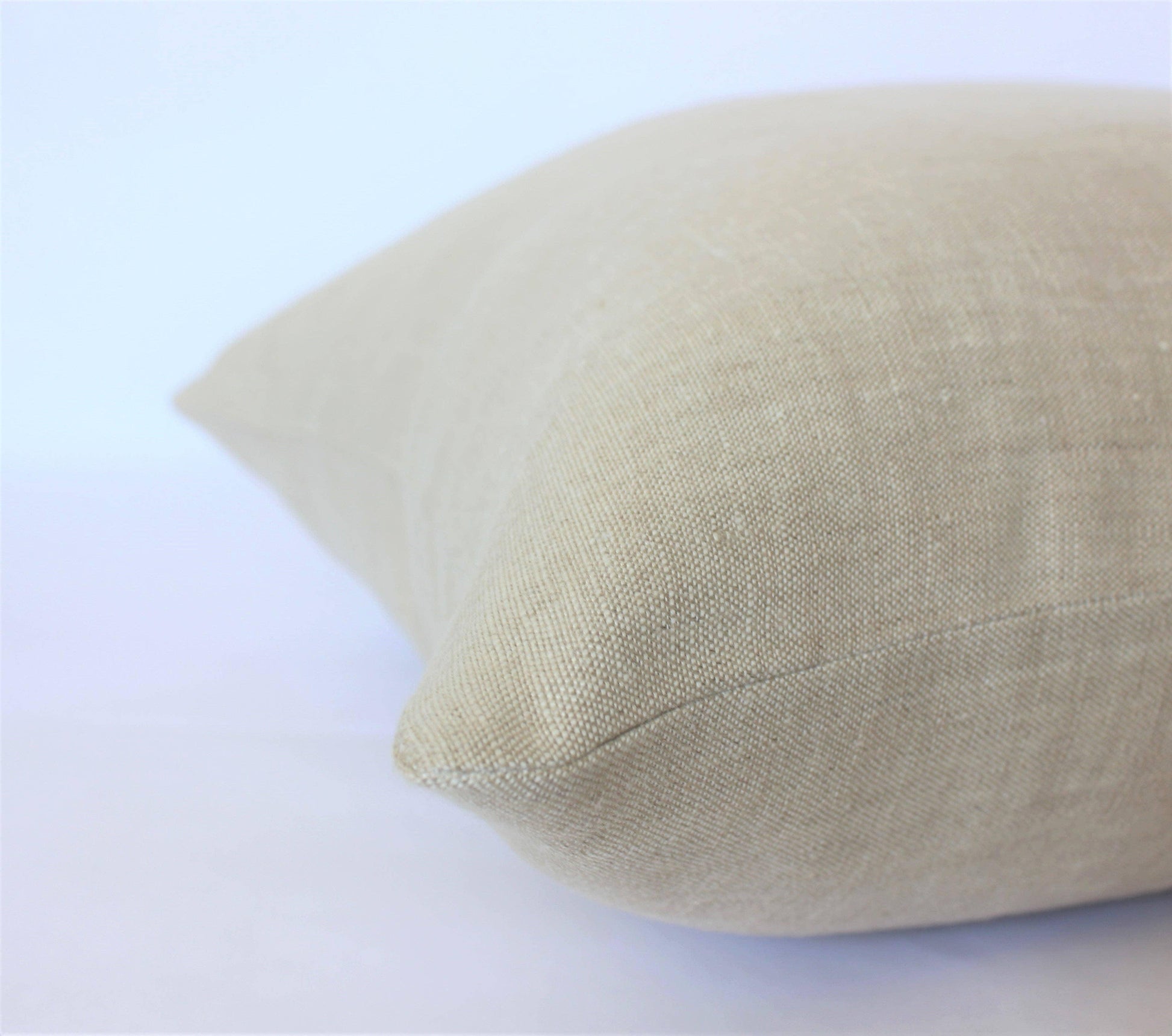 Close-up of beige linen pillow with textured fabric on white background. Come see us at Awaken, Franklin, Tennessee