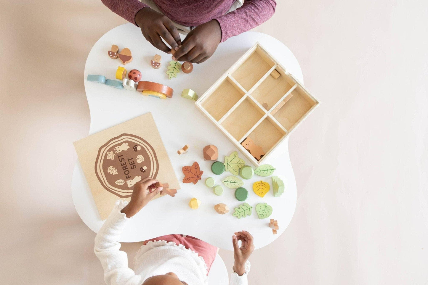 Children playing with wooden forest-themed educational toys on white table. Come see us at Awaken, Franklin, Tennessee