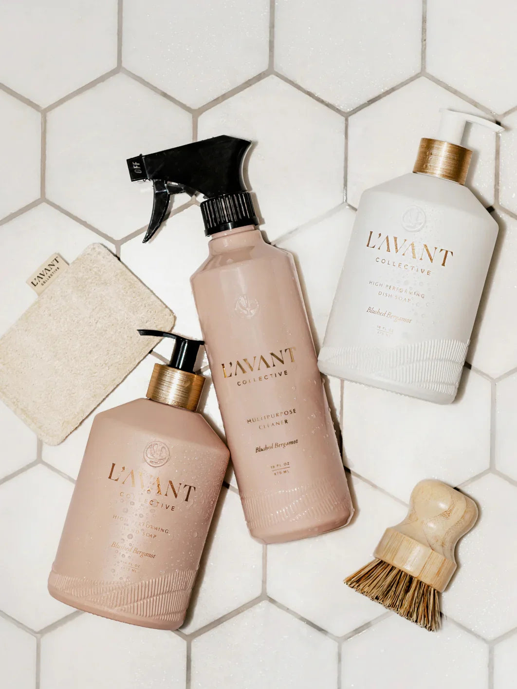 L’AVANT Collective cleaning products on white hex tile, natural sponge and brush. Come see us at Awaken, Franklin, Tennessee