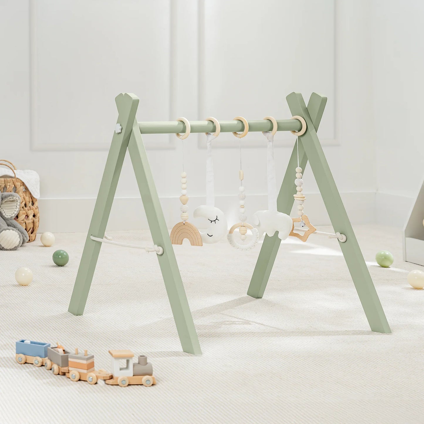 Green wooden baby gym with hanging toys and wooden train on carpet in playroom, Come see us at Awaken, Franklin, Tennessee