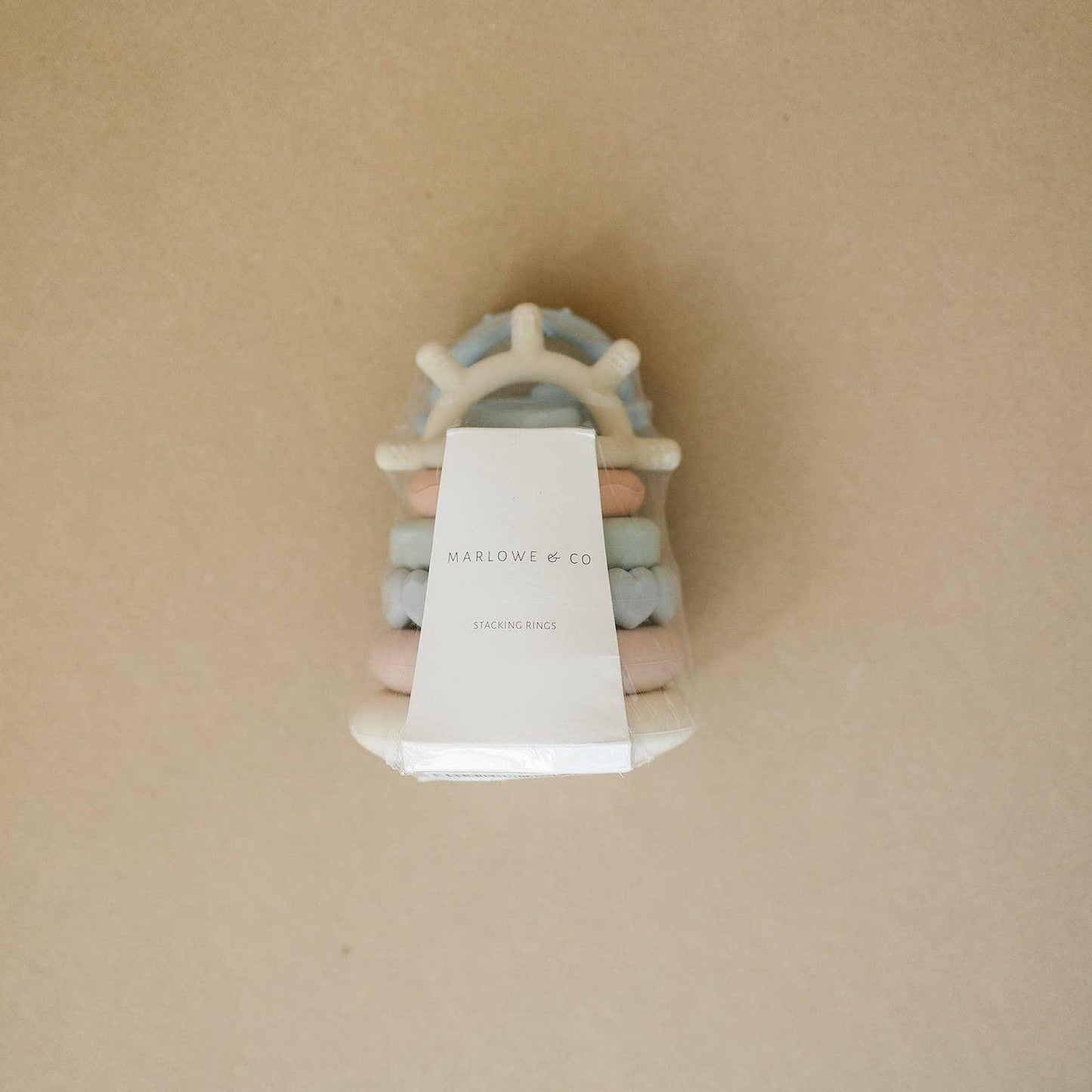 Marlowe & Co pastel-colored baby stacking rings with a steering wheel shape, on a beige background. Come see us at Awaken, Franklin, Tennessee