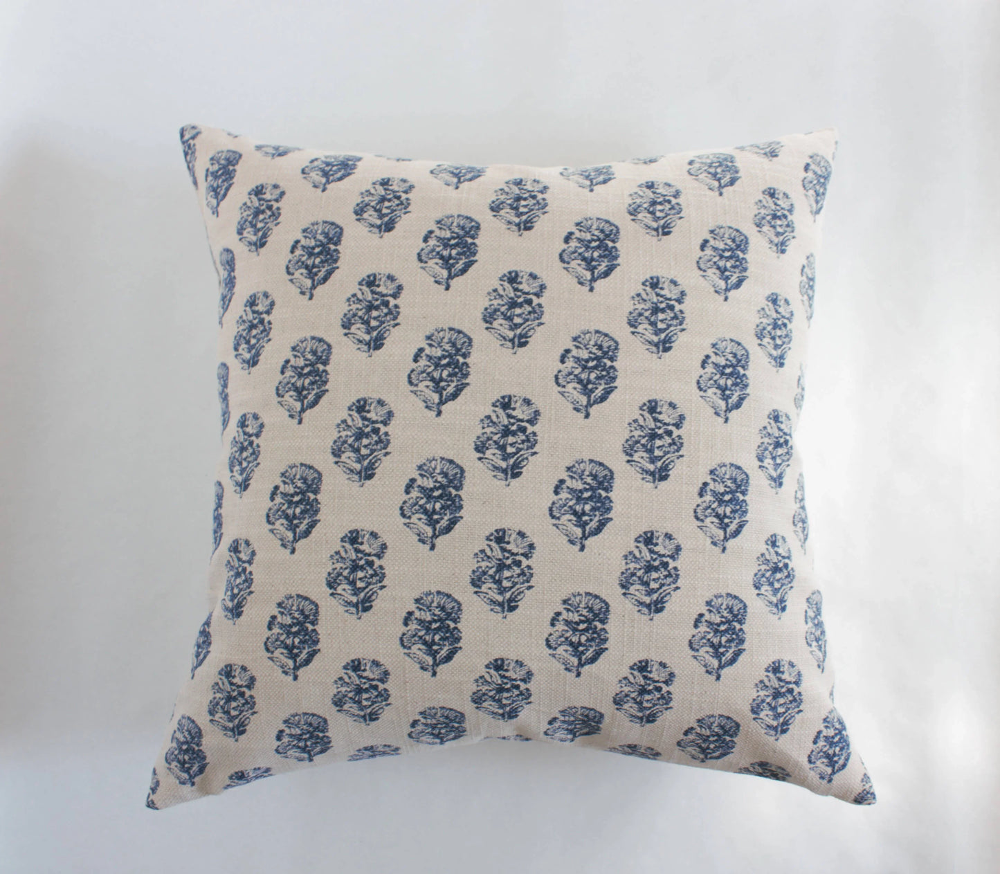 Square beige pillow with blue floral pattern on white background. Come see us at Awaken, Franklin, Tennessee