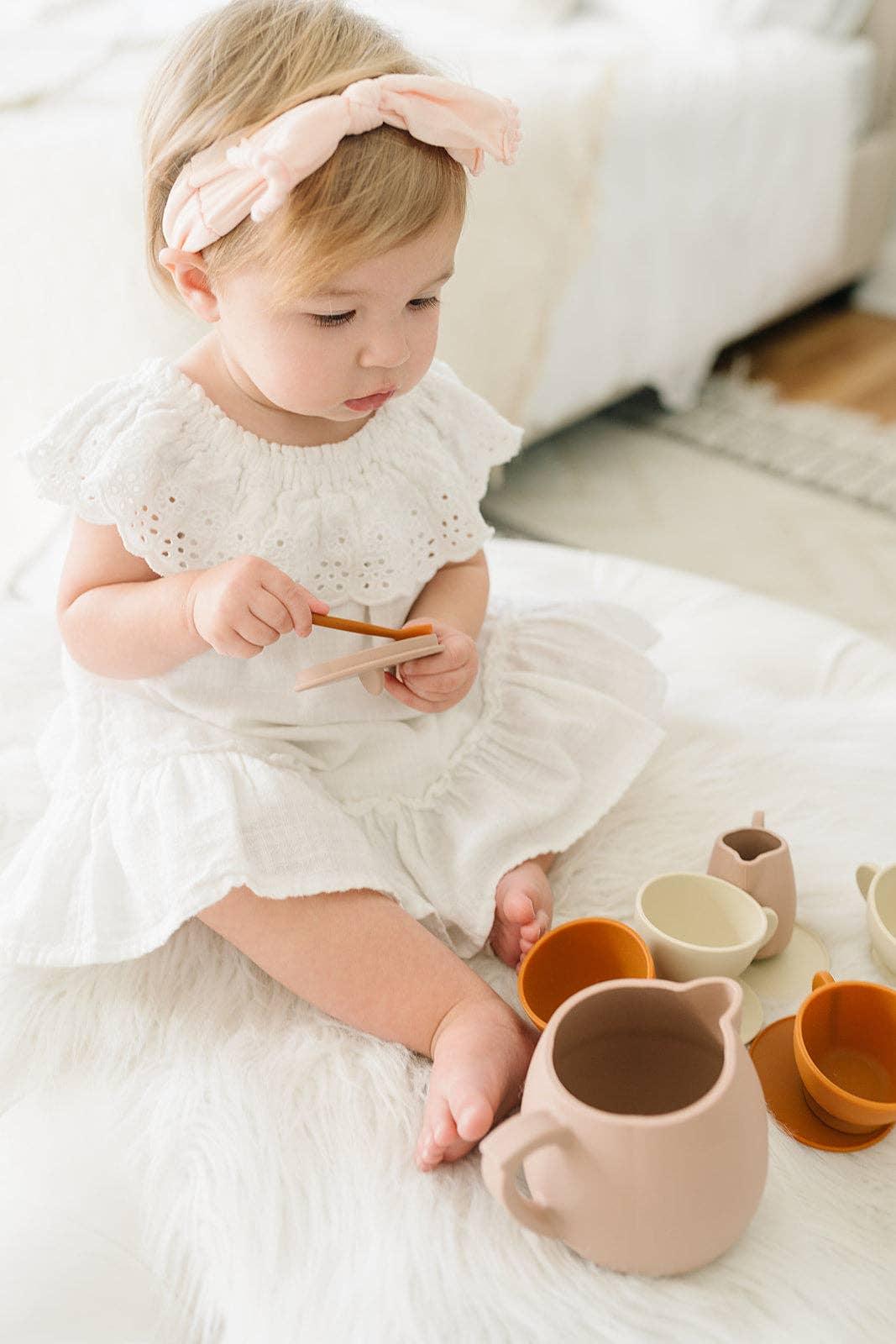Toddler in white dress and pink headband playing with tea set, Come see us at Awaken, Franklin, Tennessee