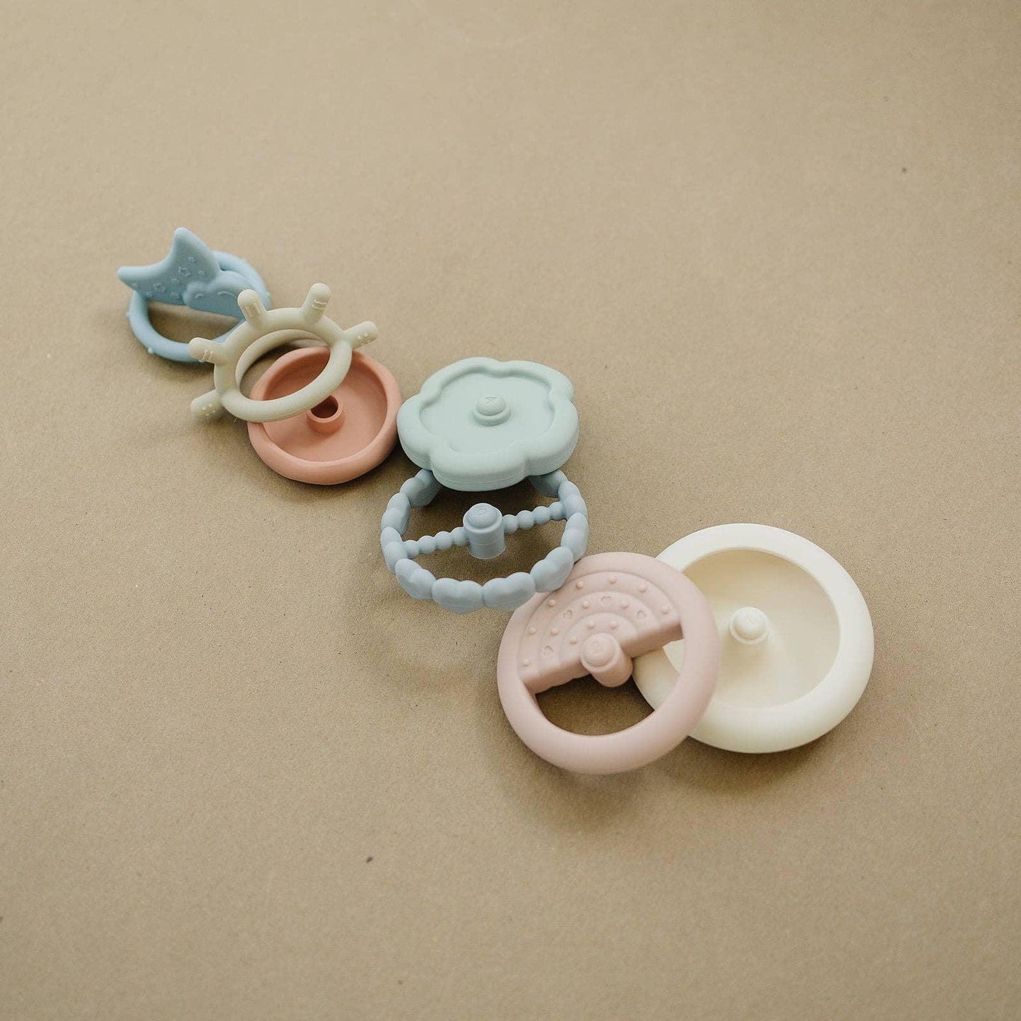 Pastel baby teether toys in unique shapes on beige background. Come see us at Awaken, Franklin, Tennessee