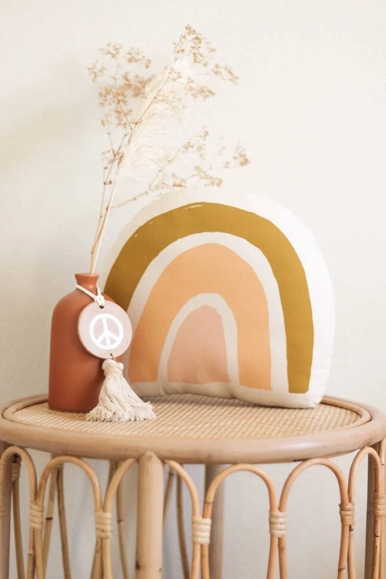 Boho decor with rainbow pillow and peace sign vase on rattan table. Come see us at Awaken, Franklin, Tennessee.