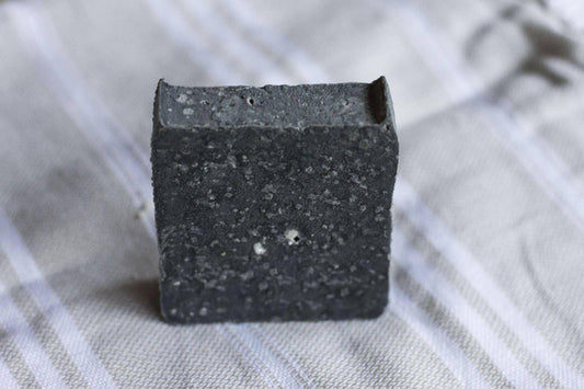 Black exfoliating soap bar with textured surface on striped fabric background. Come see us at Awaken, Franklin, Tennessee