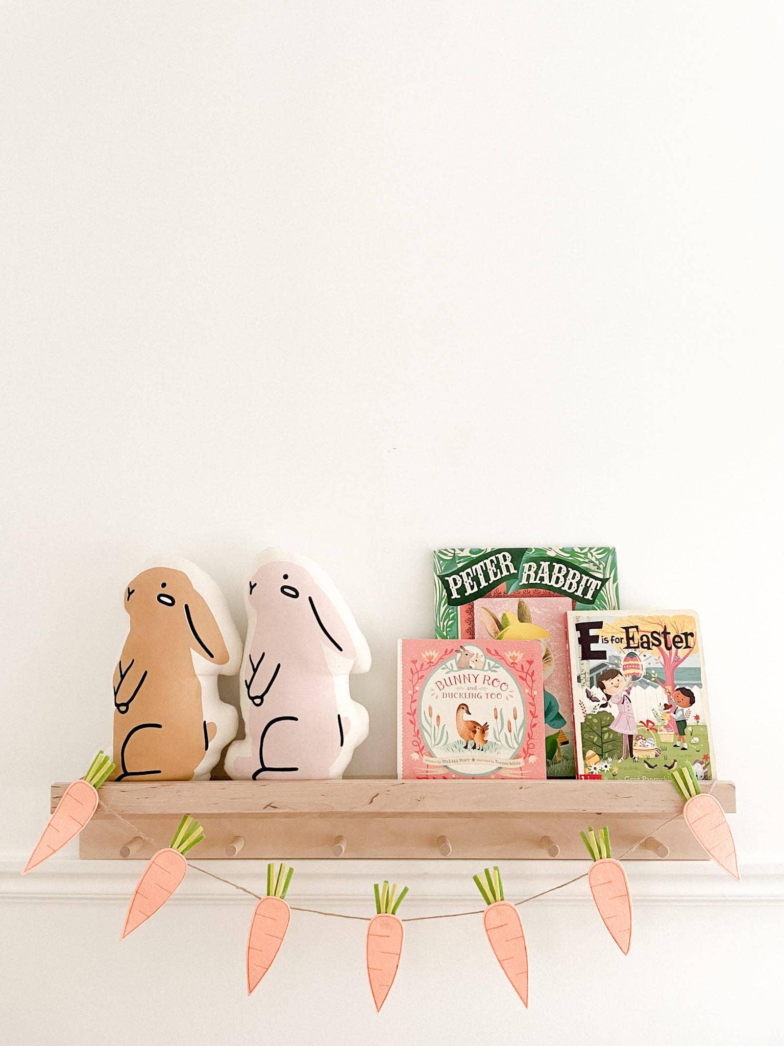 Easter bunny pillows, children's books, and carrot garland on shelf. Come see us at Awaken, Franklin, Tennessee.