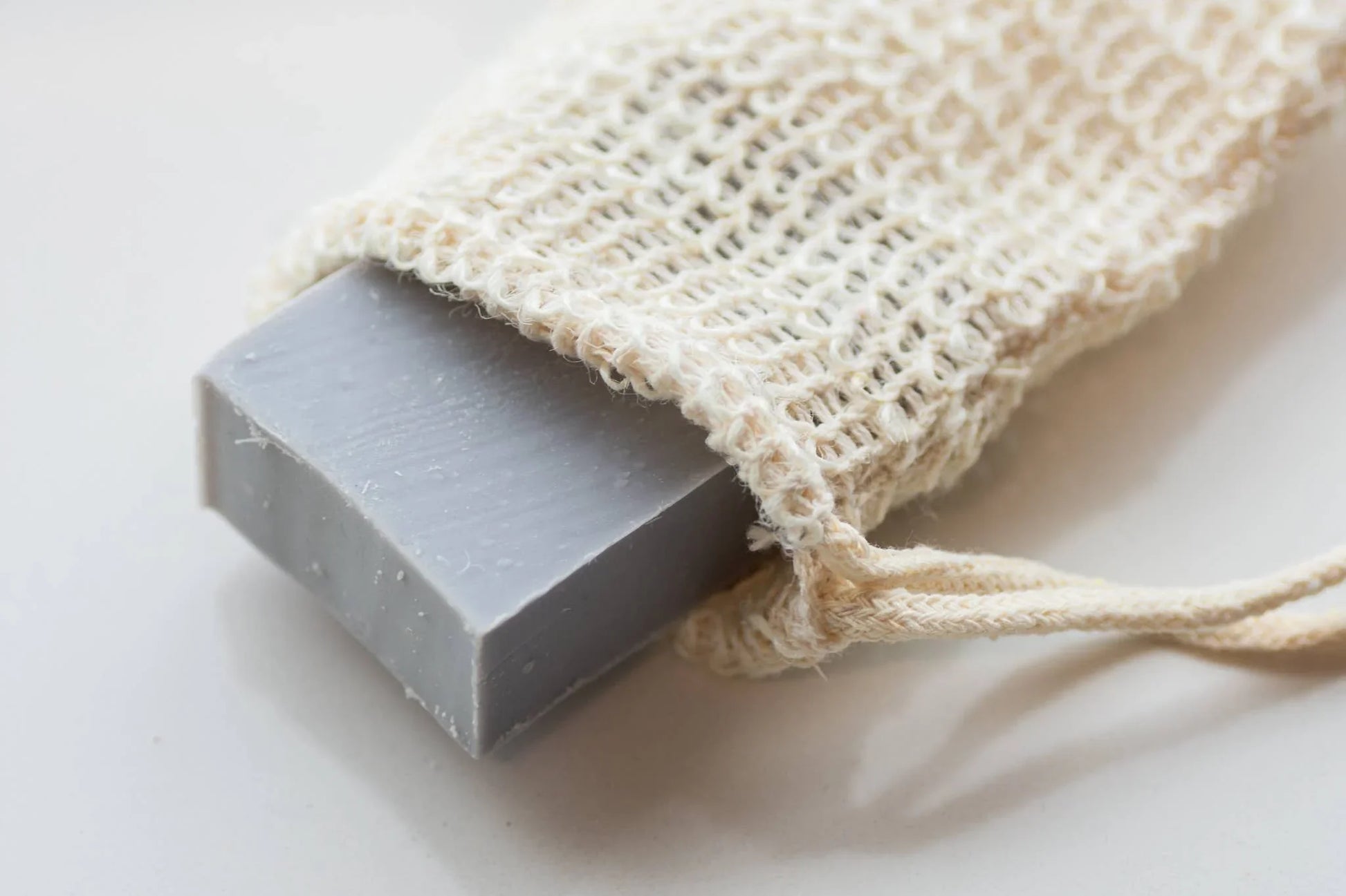 Gray soap bar in a natural woven soap saver bag on white surface, Come see us at Awaken, Franklin, Tennessee