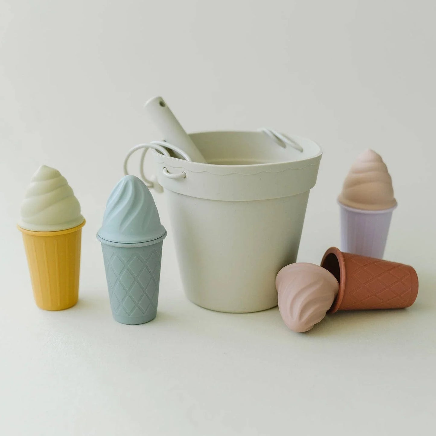 Pastel-colored toy ice cream cones and a white toy bucket with shovel on white surface. Come see us at Awaken, Franklin, Tennessee