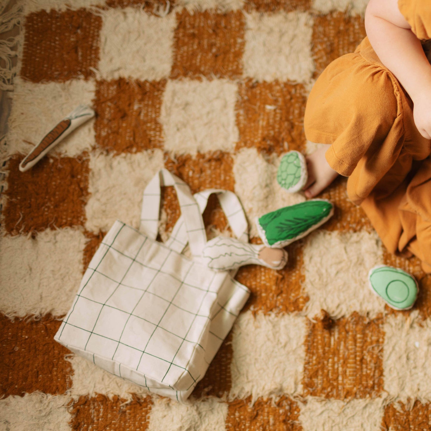 Child in orange clothes on checkered rug with tote bag and play vegetables, Come see us at Awaken, Franklin, Tennessee