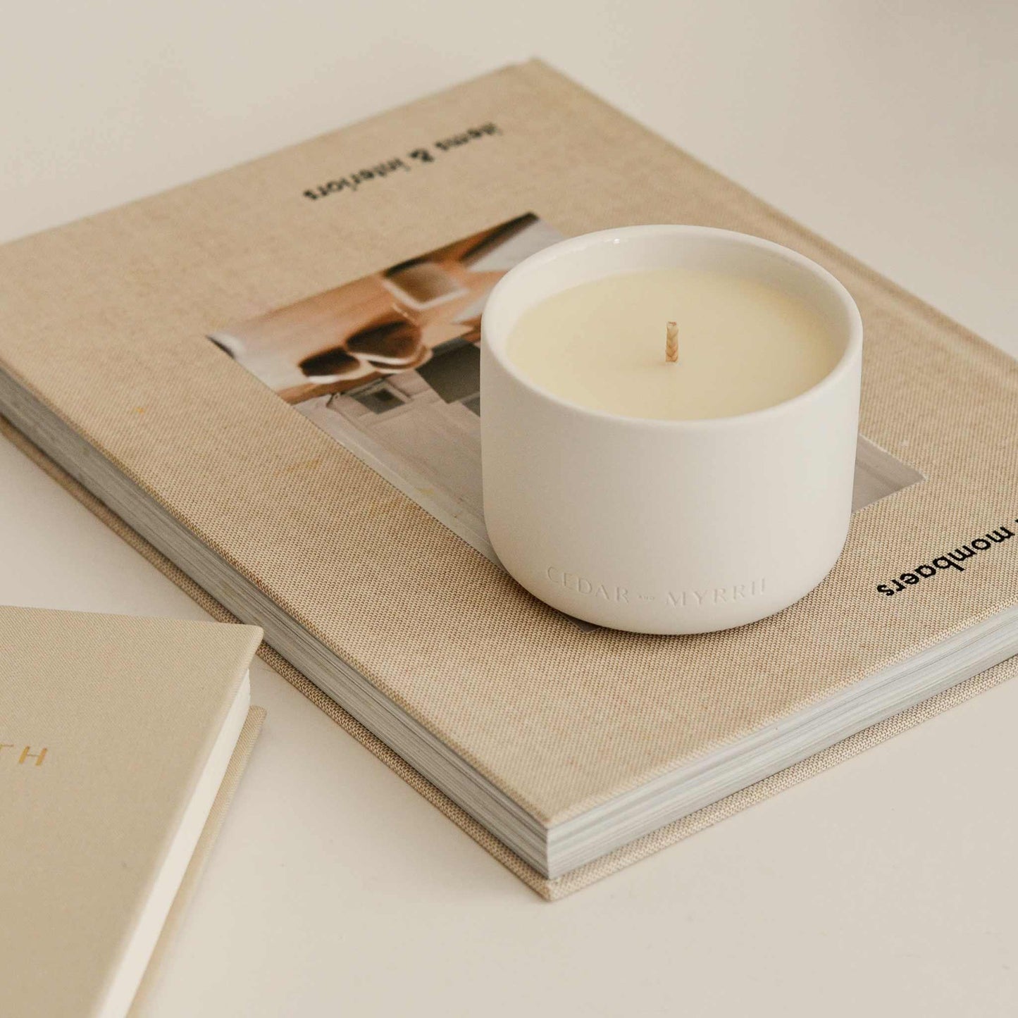 Minimalist white candle on beige books, cozy decor. Come see us at Awaken, Franklin, Tennessee.
