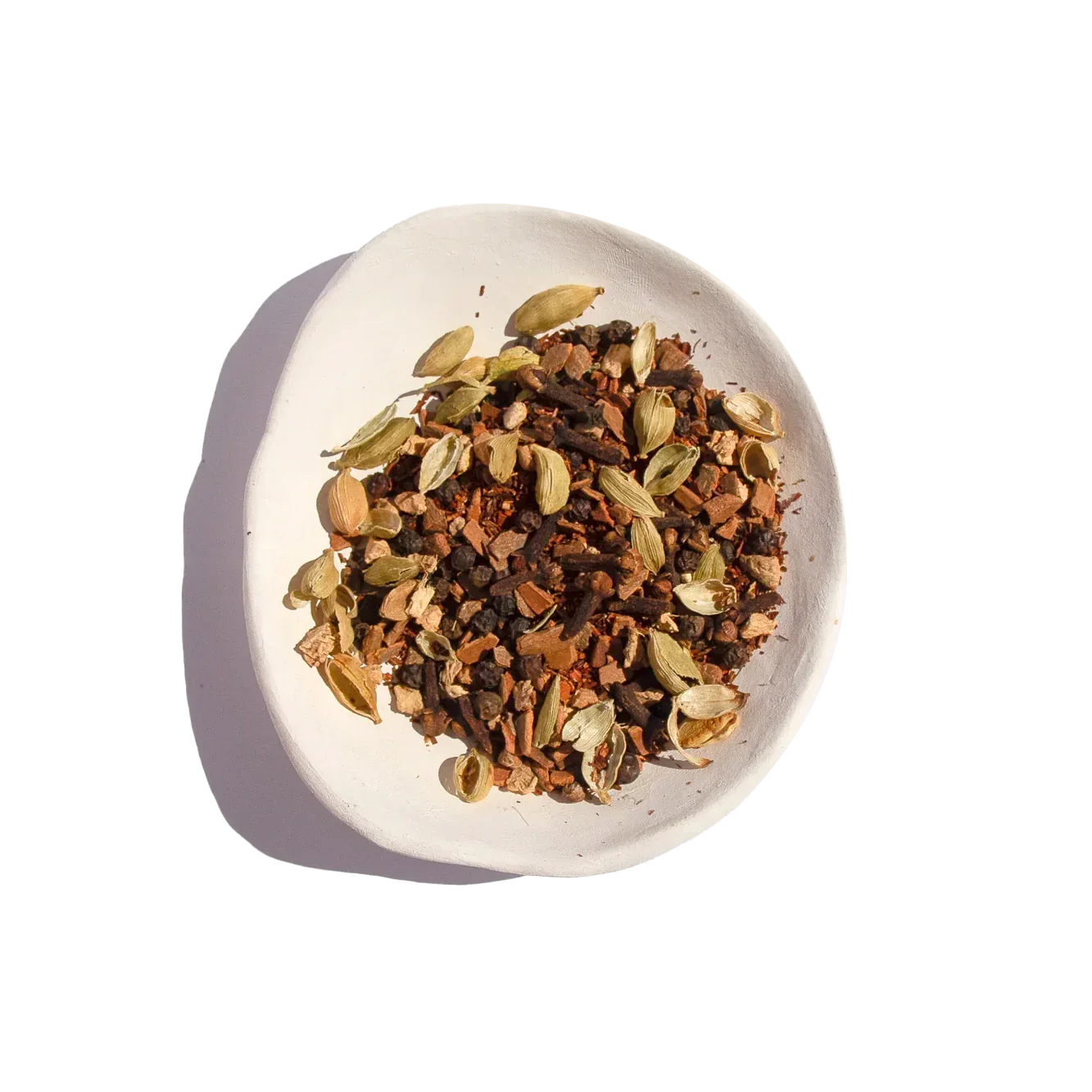 White bowl with mixed dried chai spices including cardamom, cloves, cinnamon, and peppercorns. Come see us at Awaken, Franklin, Tennessee