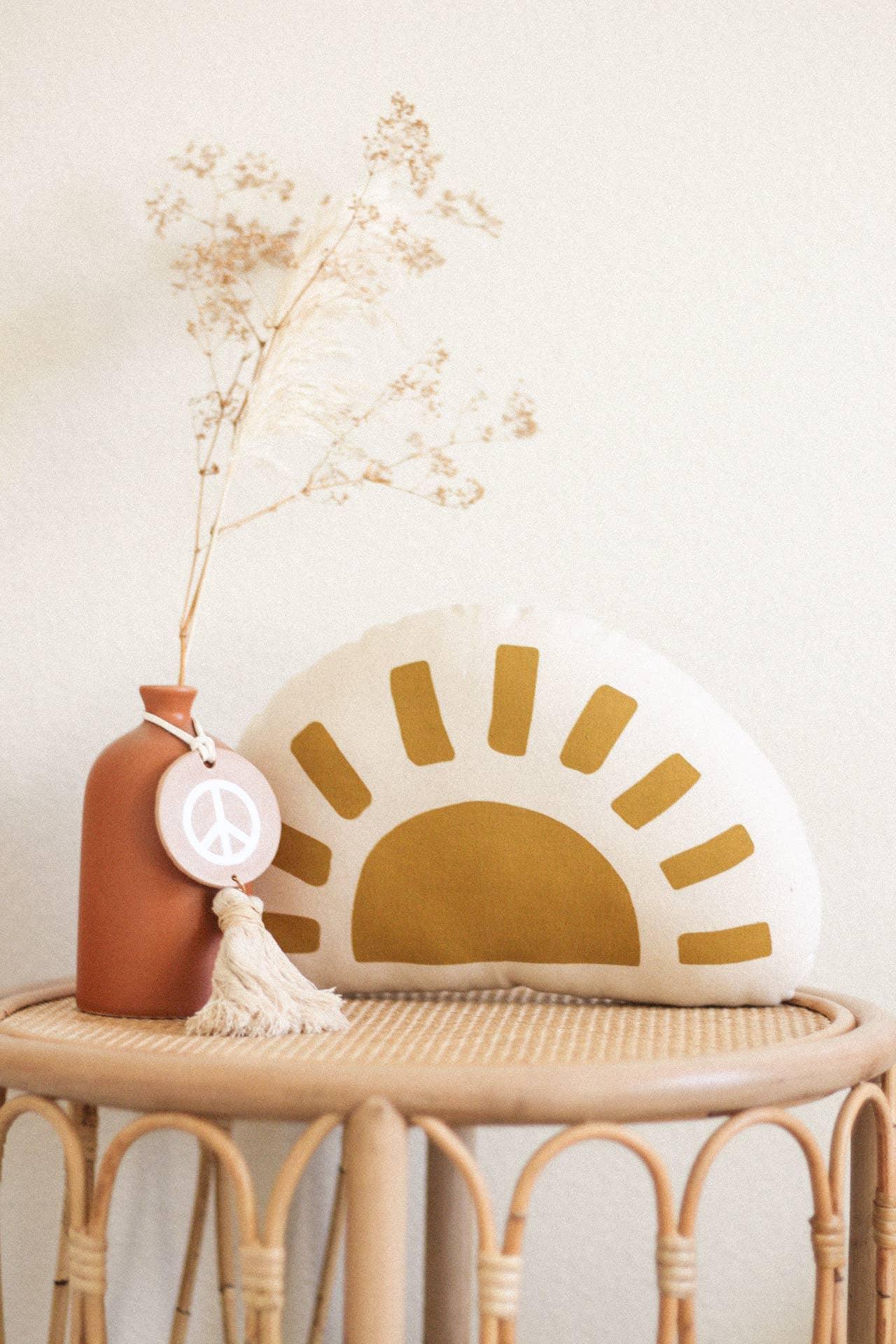 Boho decor with sun pillow, dried flowers, peace tag on wicker table. Come see us at Awaken, Franklin, Tennessee