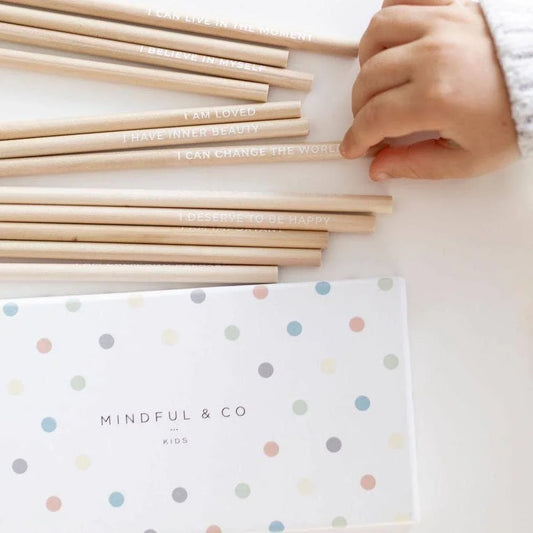 Child's hand holding motivational wooden pencils with positive messages and Mindful & Co Kids box. Come see us at Awaken, Franklin, Tennessee