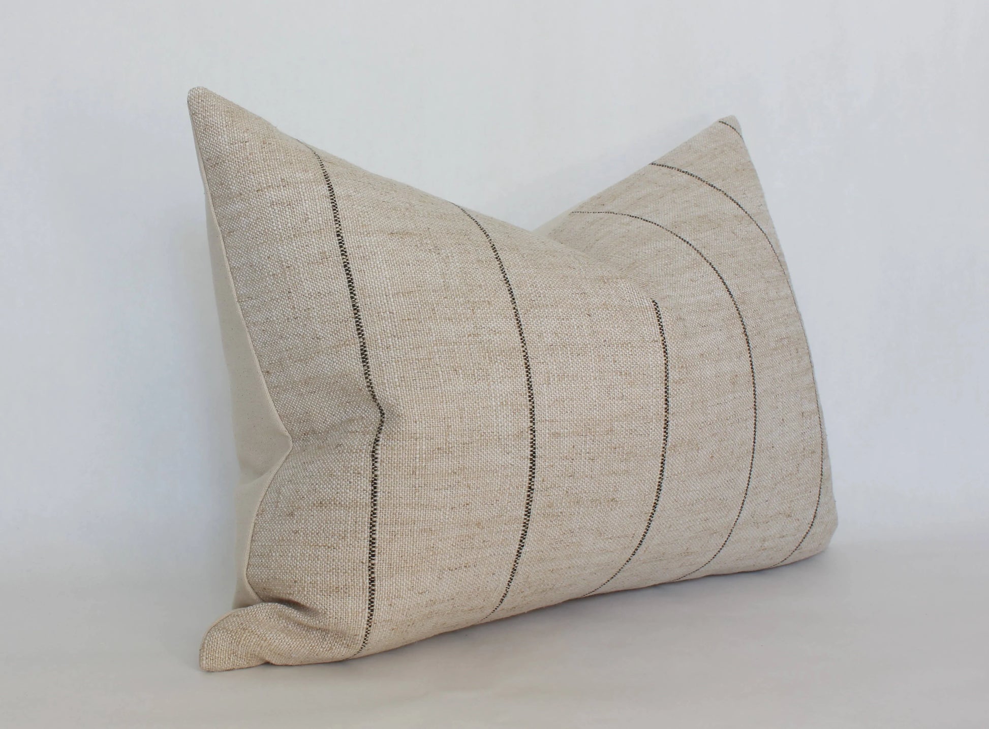Natural beige lumbar pillow with subtle black stripes on white background. Come see us at Awaken, Franklin, Tennessee