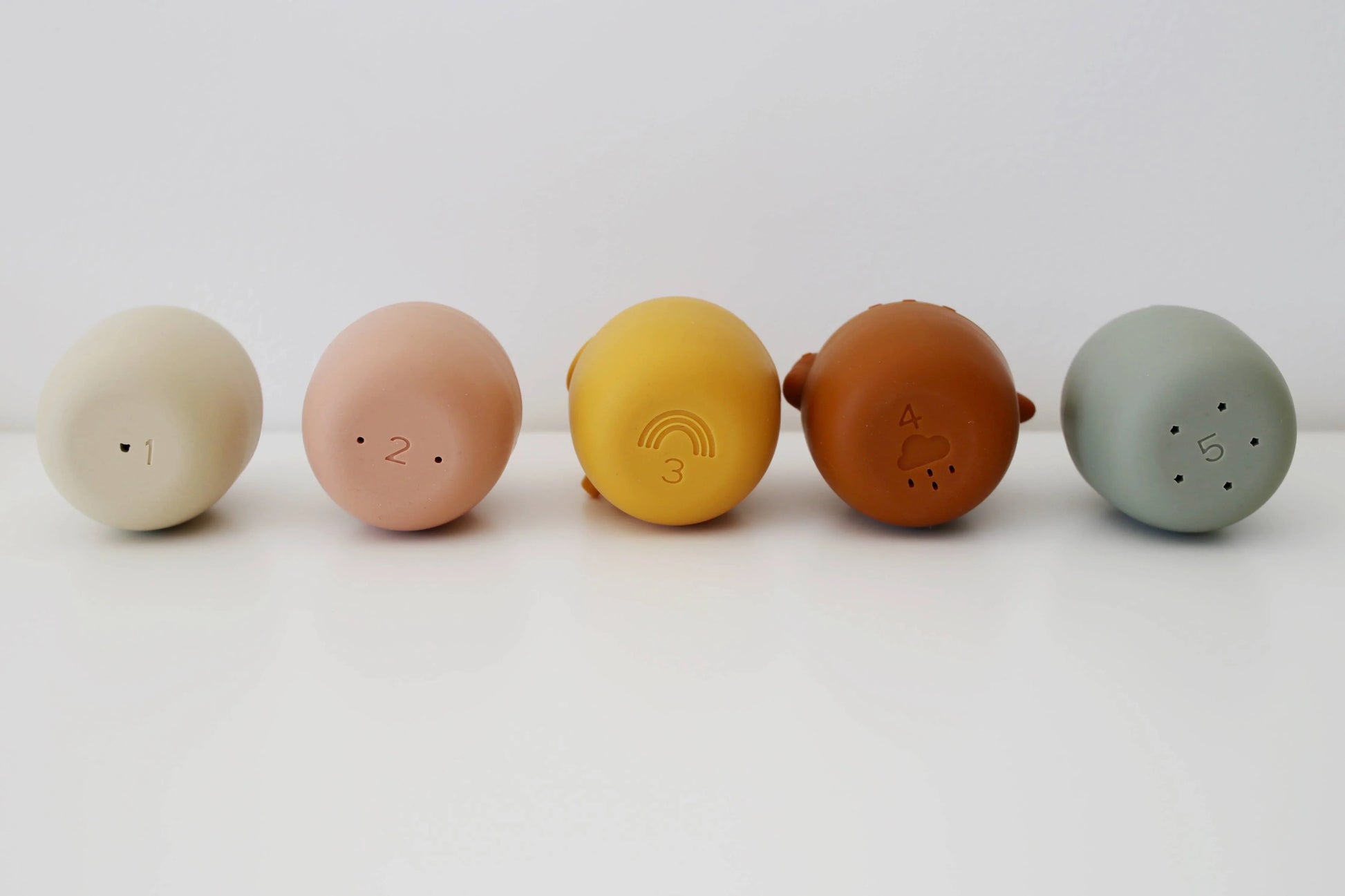 Five pastel-colored round baby toys numbered 1 to 5 with nature motifs on white surface. Come see us at Awaken, Franklin, Tennessee