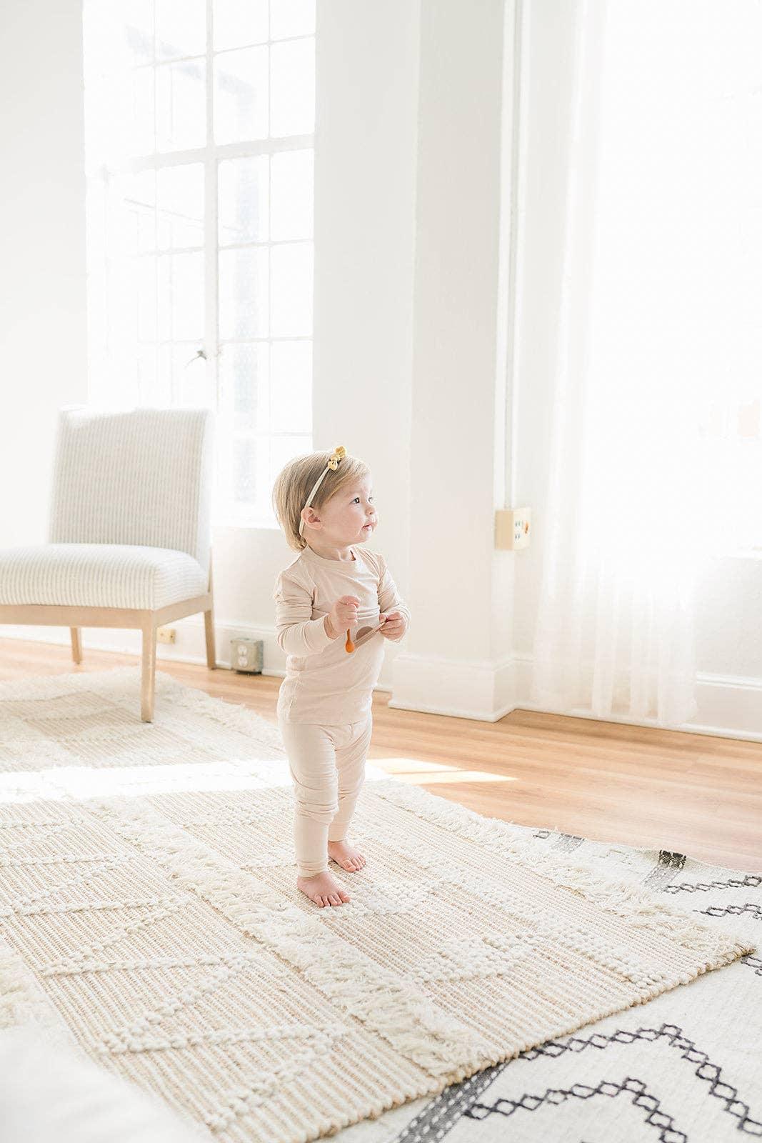 Baby in beige outfit standing on textured rug in bright room, Come see us at Awaken, Franklin, Tennessee