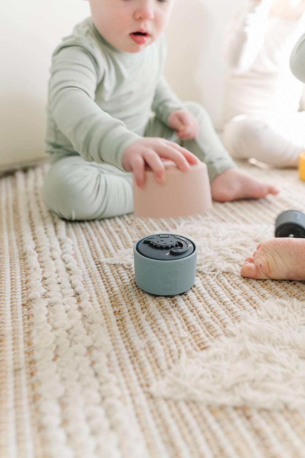 Toddler in green pajamas playing with stacking cups on textured rug, Come see us at Awaken, Franklin, Tennessee