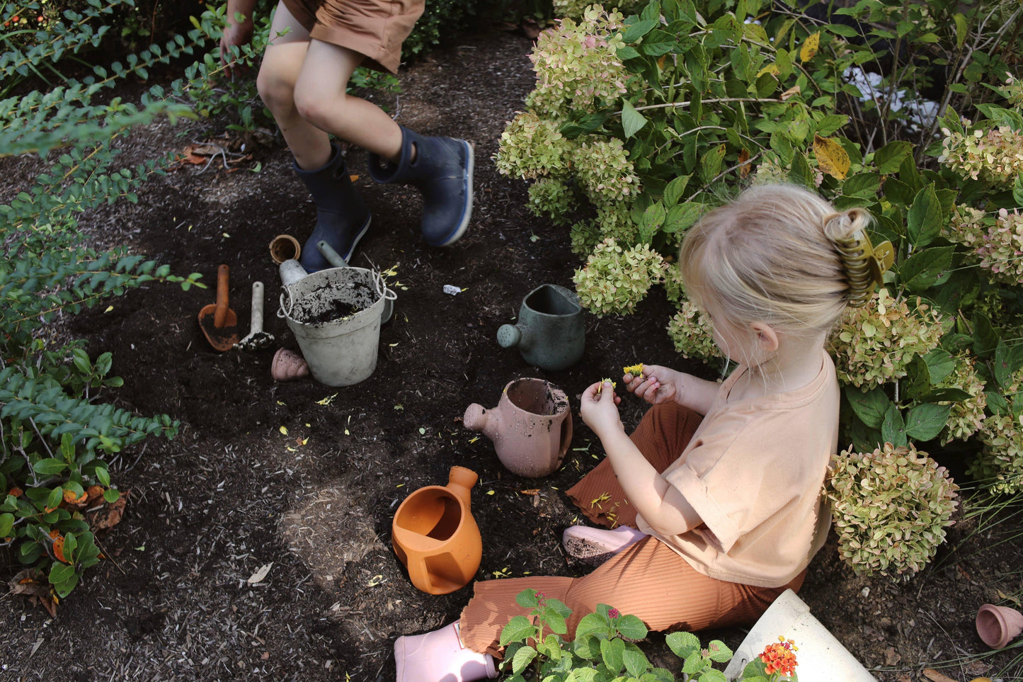 Children gardening with soil, watering cans, and tools among green plants and flowers. Come see us at Awaken, Franklin, Tennessee