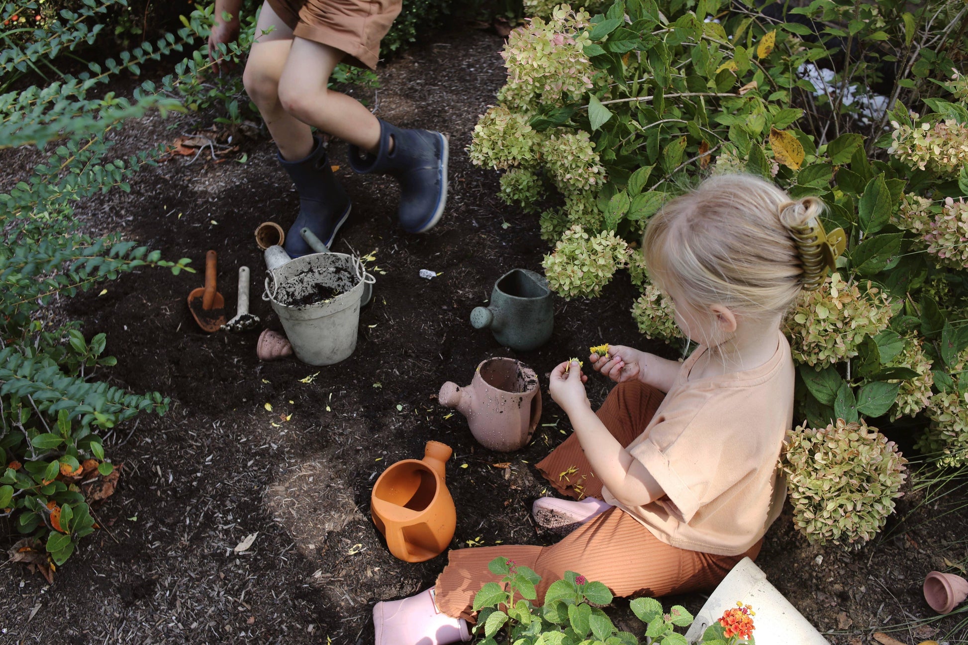 Children gardening with soil, watering cans, and tools among green plants and flowers. Come see us at Awaken, Franklin, Tennessee