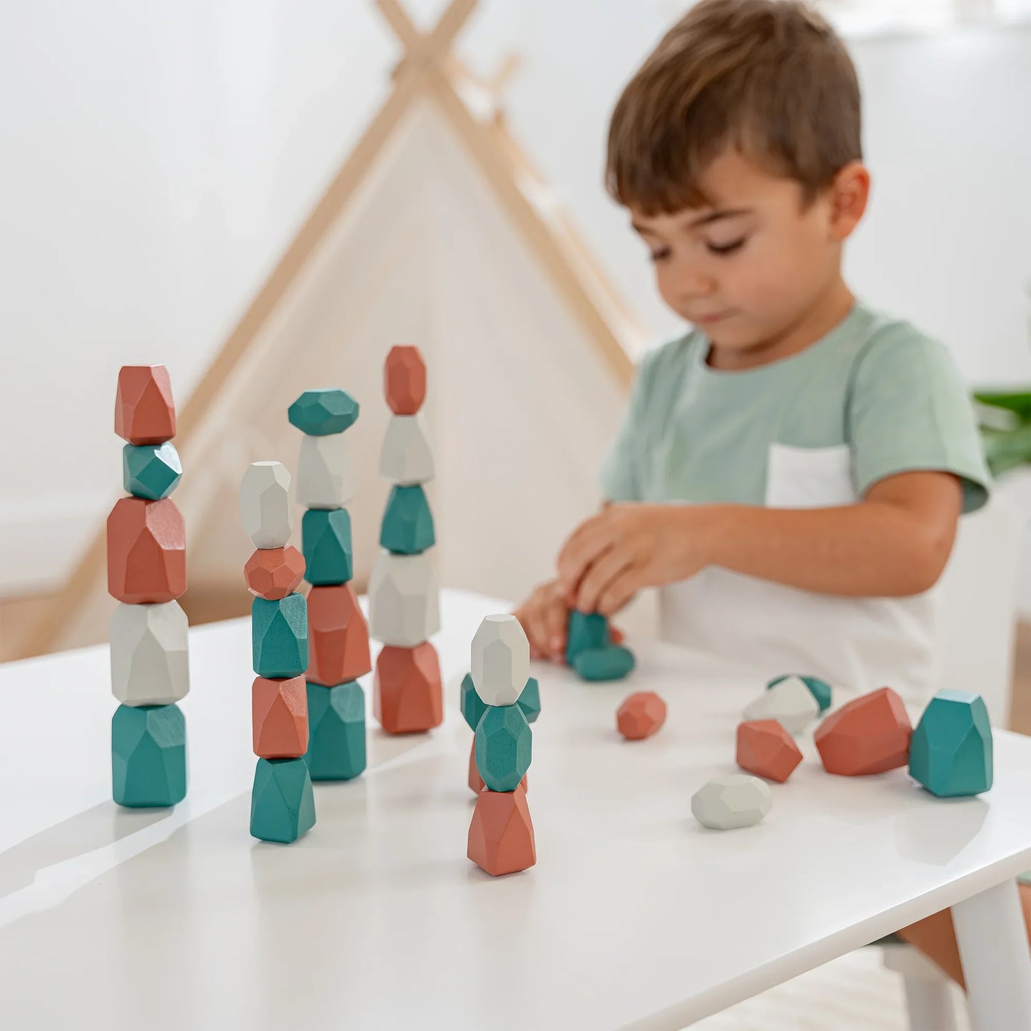 Child playing with colorful wooden stacking blocks on white table in bright room Come see us at Awaken, Franklin, Tennessee
