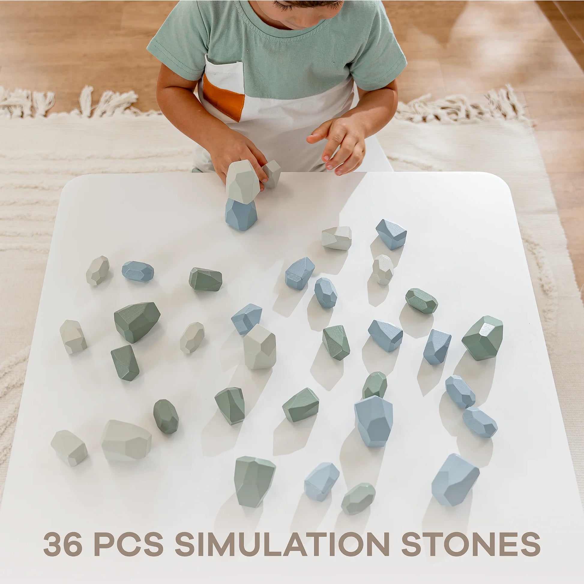 Child playing with 36-piece set of blue and green simulation stones on white table - Come see us at Awaken, Franklin, Tennessee