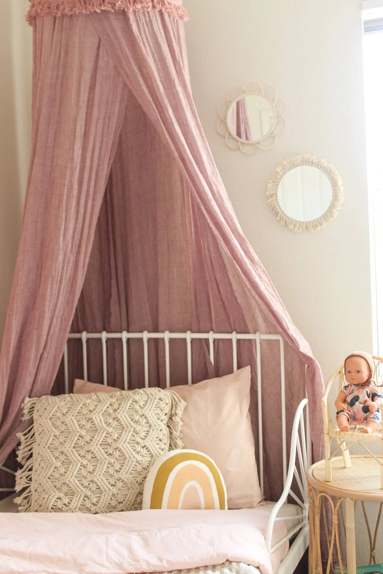 Boho kids bedroom with pink canopy, macrame pillow, rainbow cushion, mirrors, and doll. Come see us at Awaken, Franklin, Tennessee.