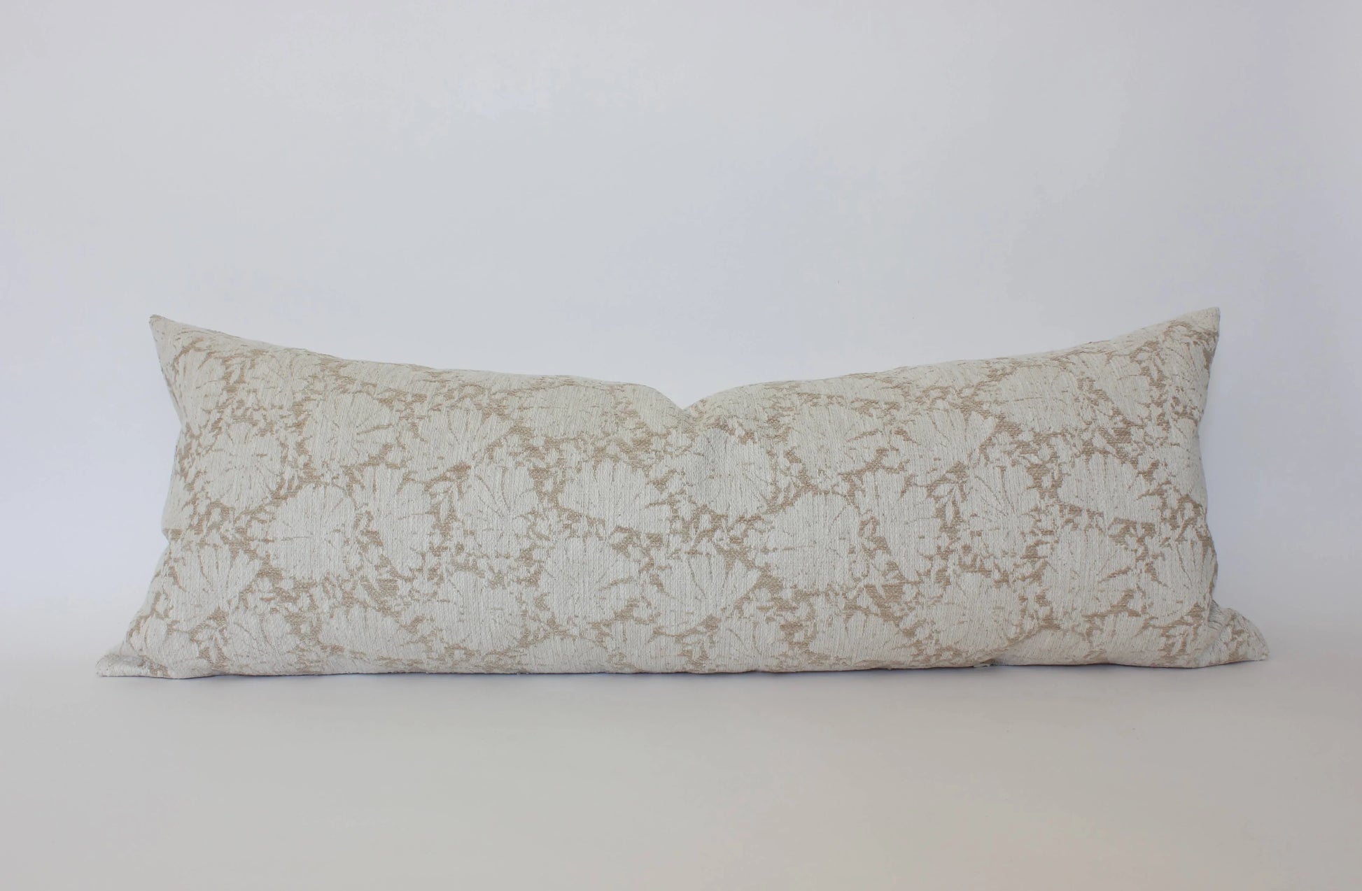 Long lumbar pillow with beige floral pattern on white background. Come see us at Awaken, Franklin, Tennessee