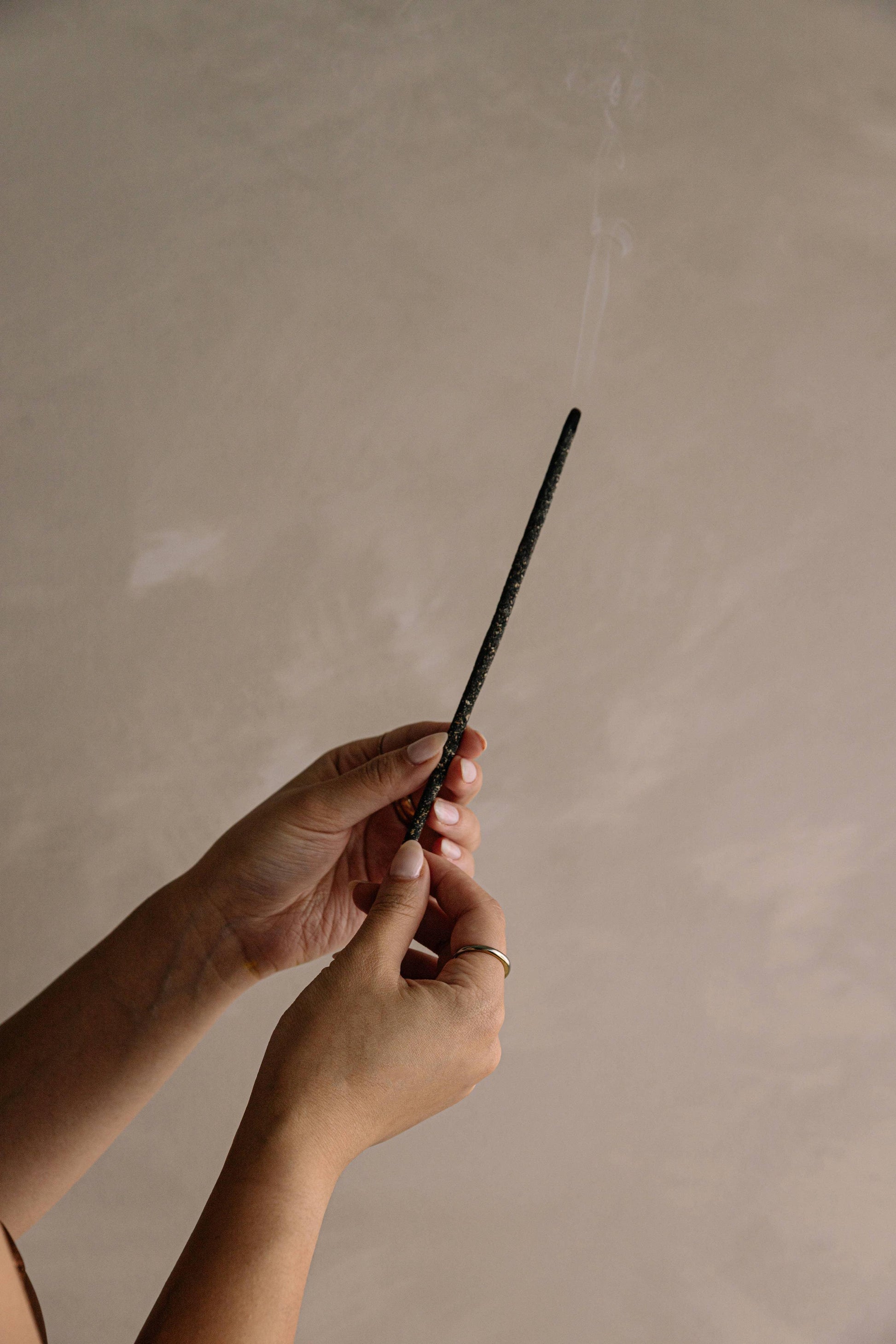 Hands holding a burning black incense stick with smoke against a neutral background. Come see us at Awaken, Franklin, Tennessee