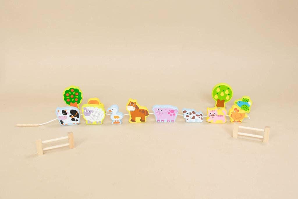 Wooden farm animal pull toy with cow, sheep, horse, pig, dog, cat, duck, trees on beige background. Come see us at Awaken, Franklin, Tennessee