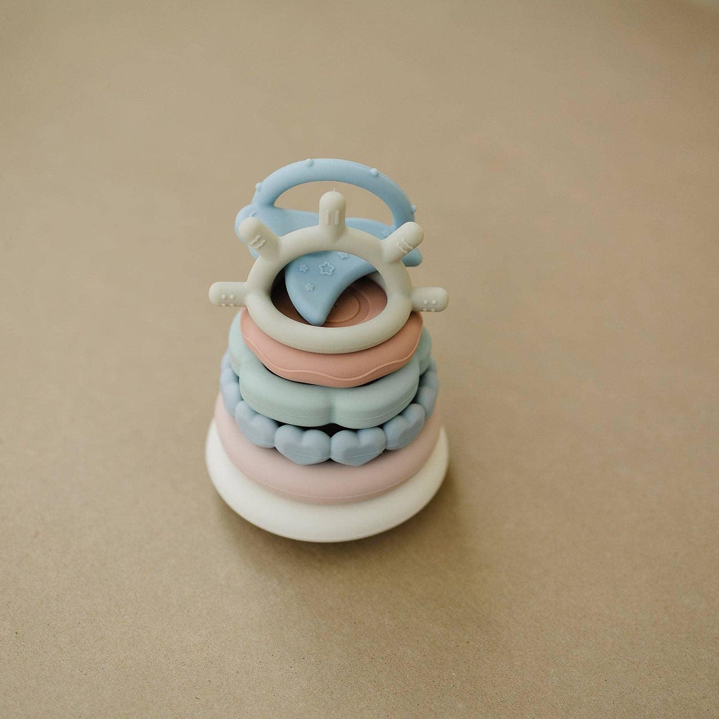 Stack of pastel-colored silicone baby toys with various shapes on beige surface. Come see us at Awaken, Franklin, Tennessee