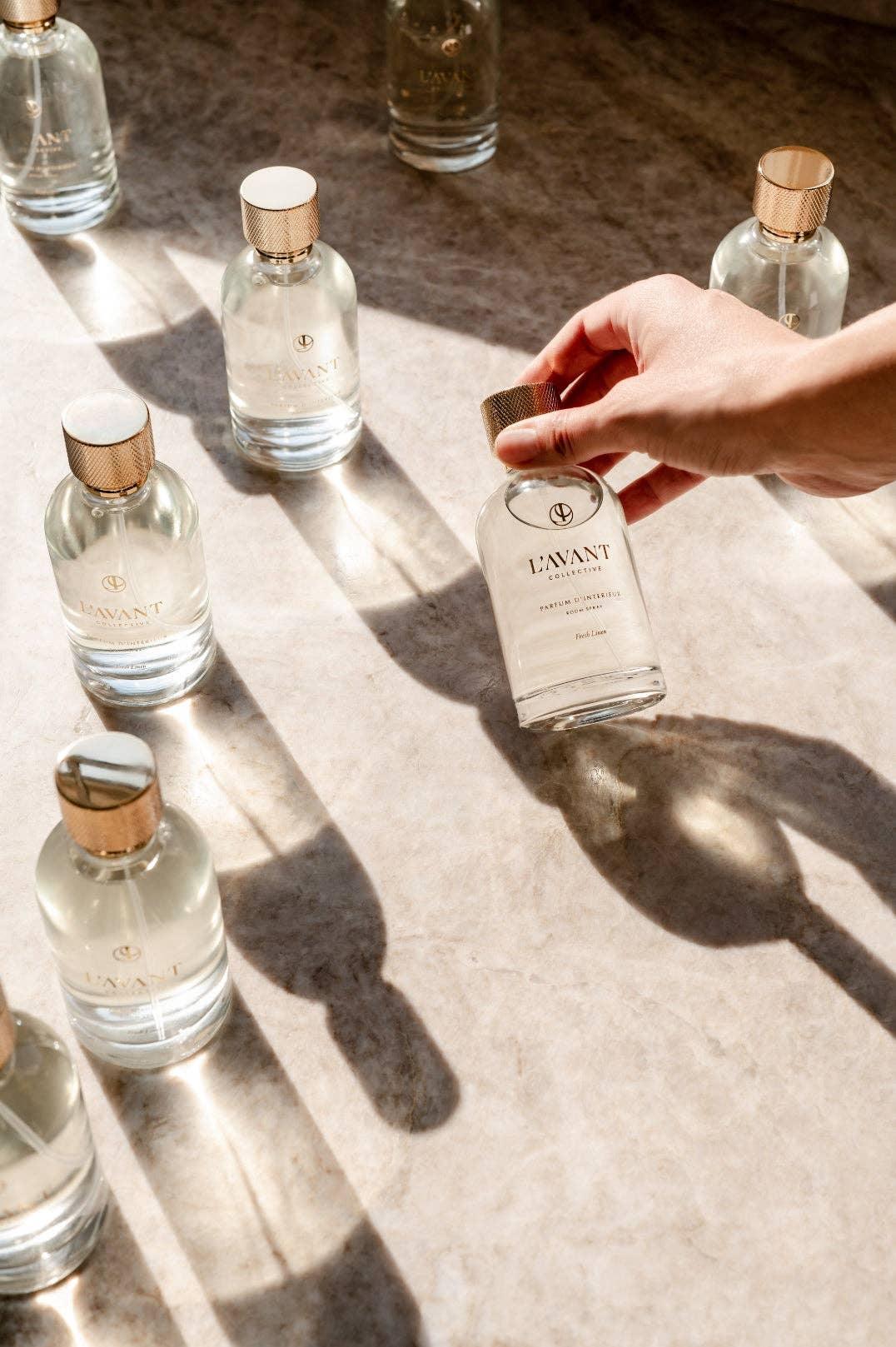 Hand picking up L'AVANT Collective glass bottle on marble surface, sunlit, Come see us at Awaken, Franklin, Tennessee