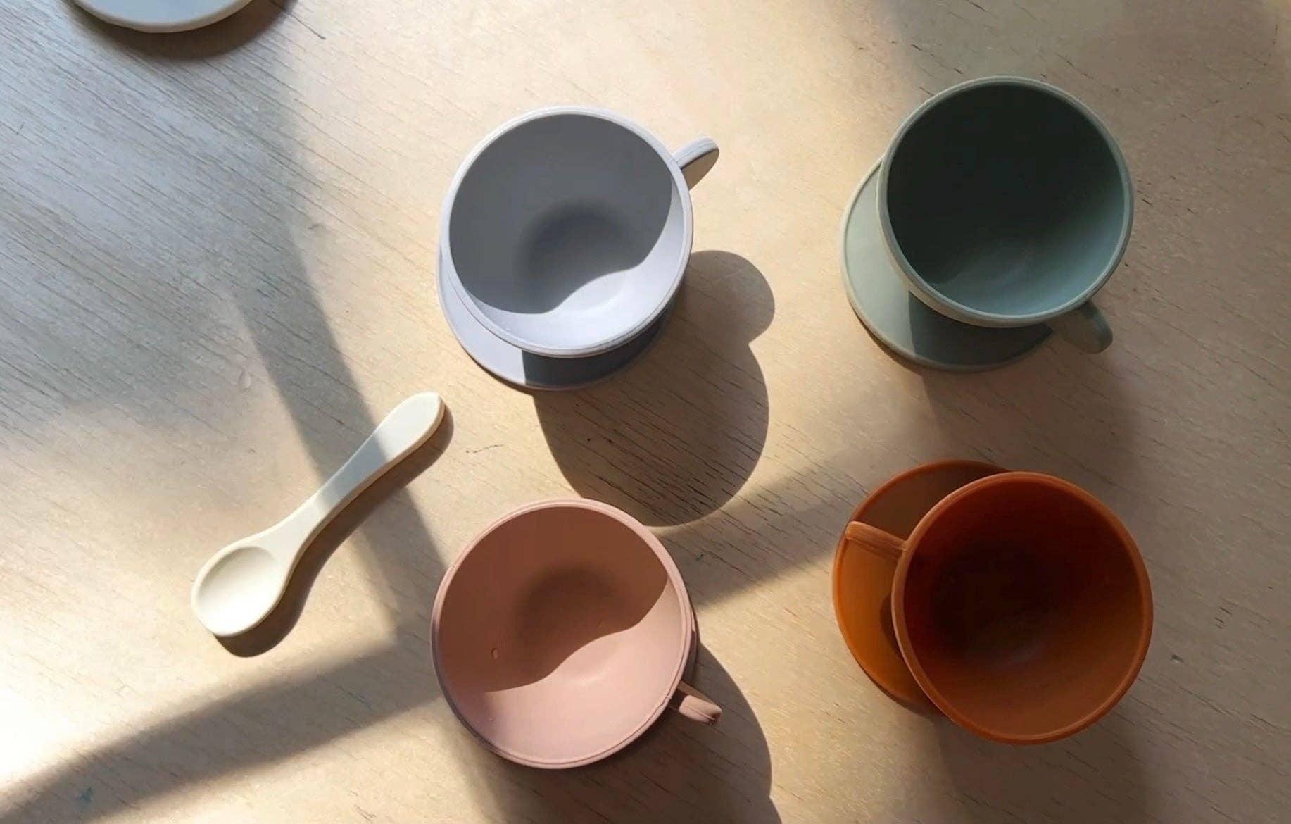 Colorful ceramic cups and a spoon on a wooden table in sunlight. Come see us at Awaken, Franklin, Tennessee.