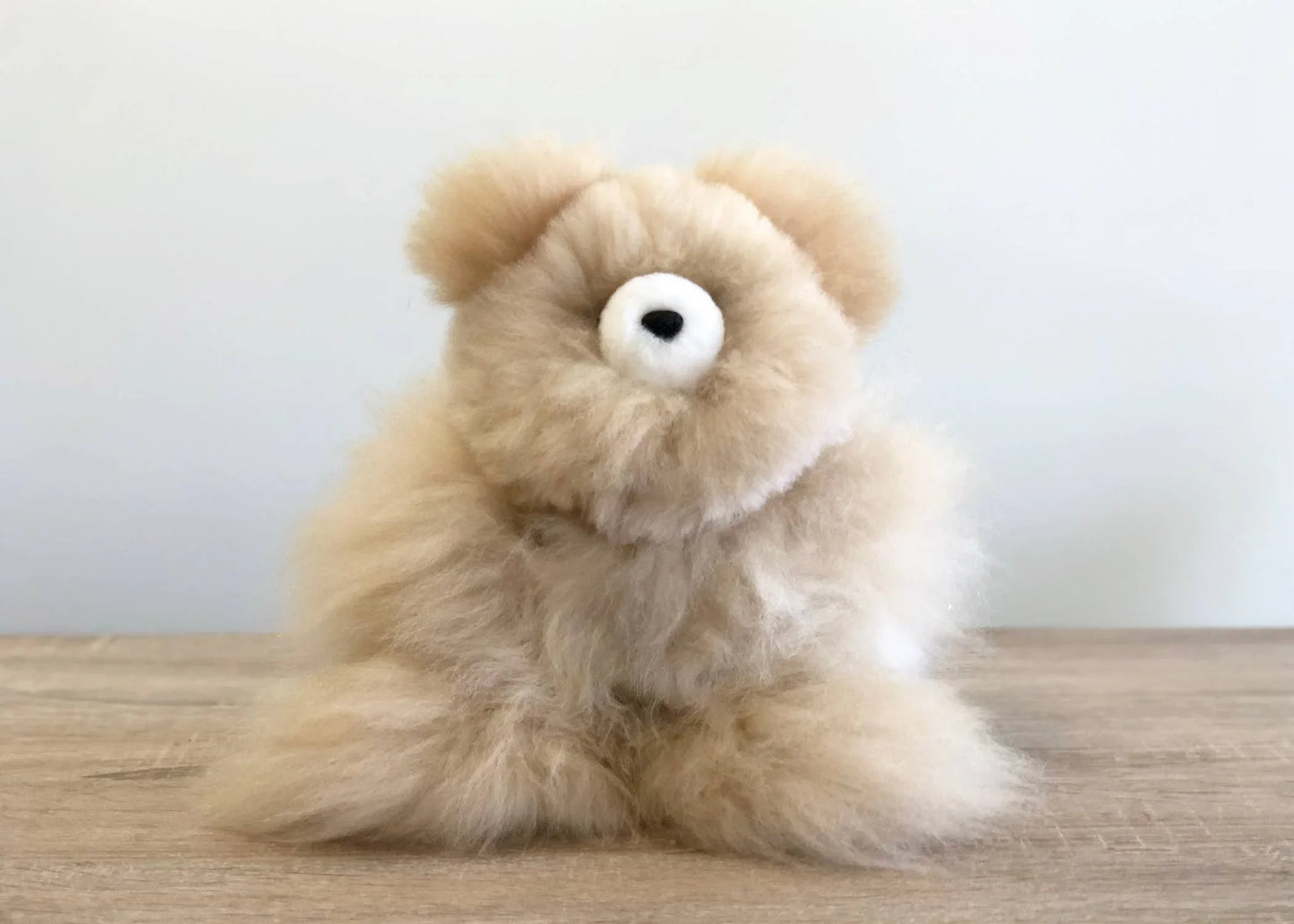Fluffy beige teddy bear plush on wooden table with plain white background. Come see us at Awaken, Franklin, Tennessee