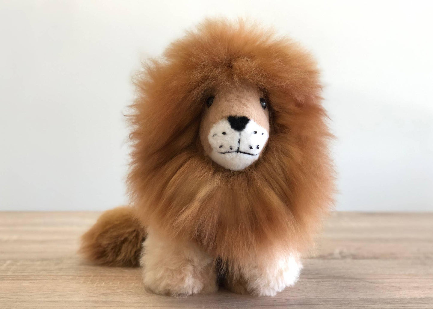 Plush felt lion with fluffy mane on wooden surface, white background. Come see us at Awaken, Franklin, Tennessee