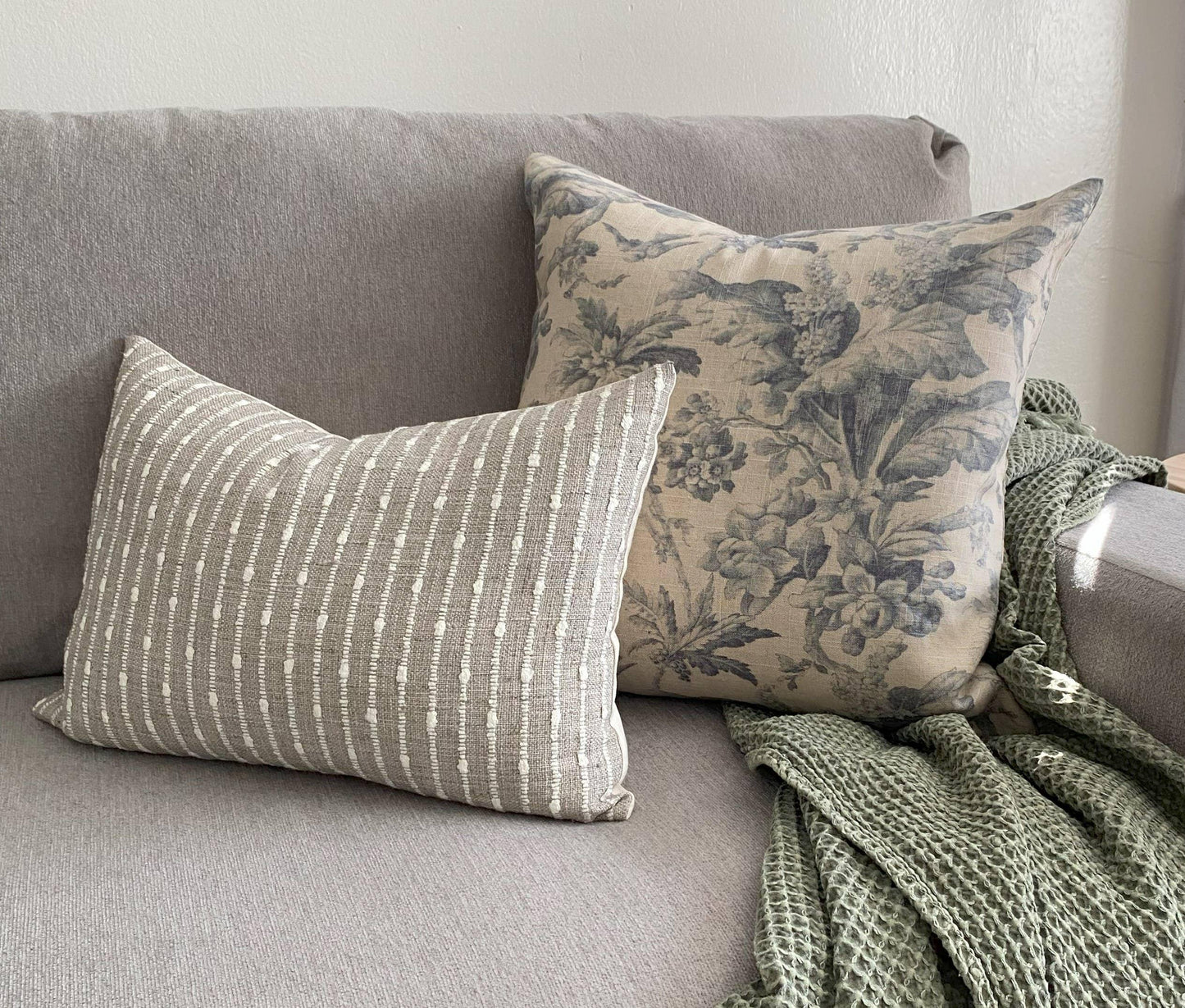 Grey sofa with striped and floral decorative pillows and a green textured throw blanket. Come see us at Awaken, Franklin, Tennessee