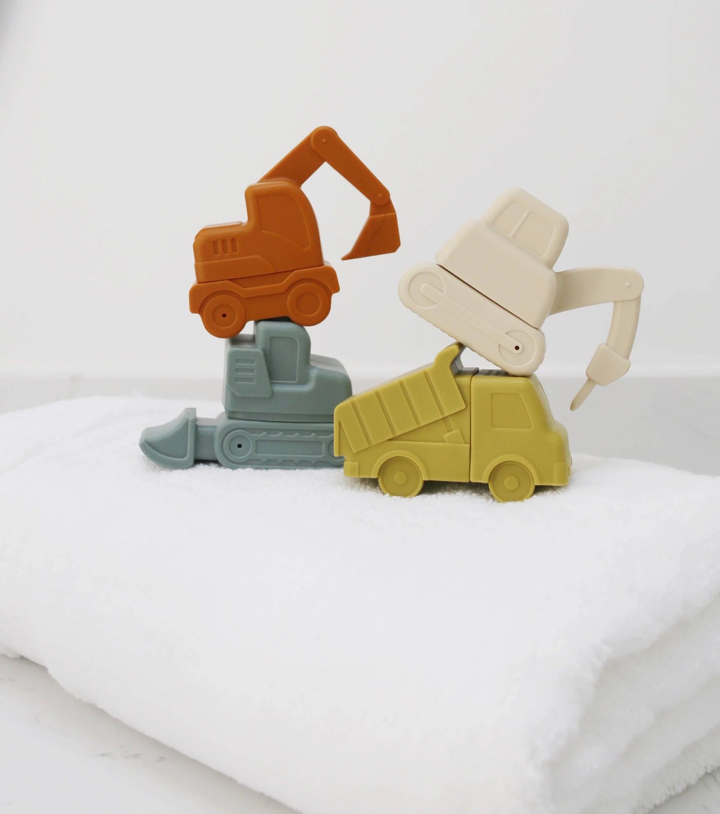 Stacked colorful silicone toy construction vehicles on white towel, minimalist background. Come see us at Awaken, Franklin, Tennessee