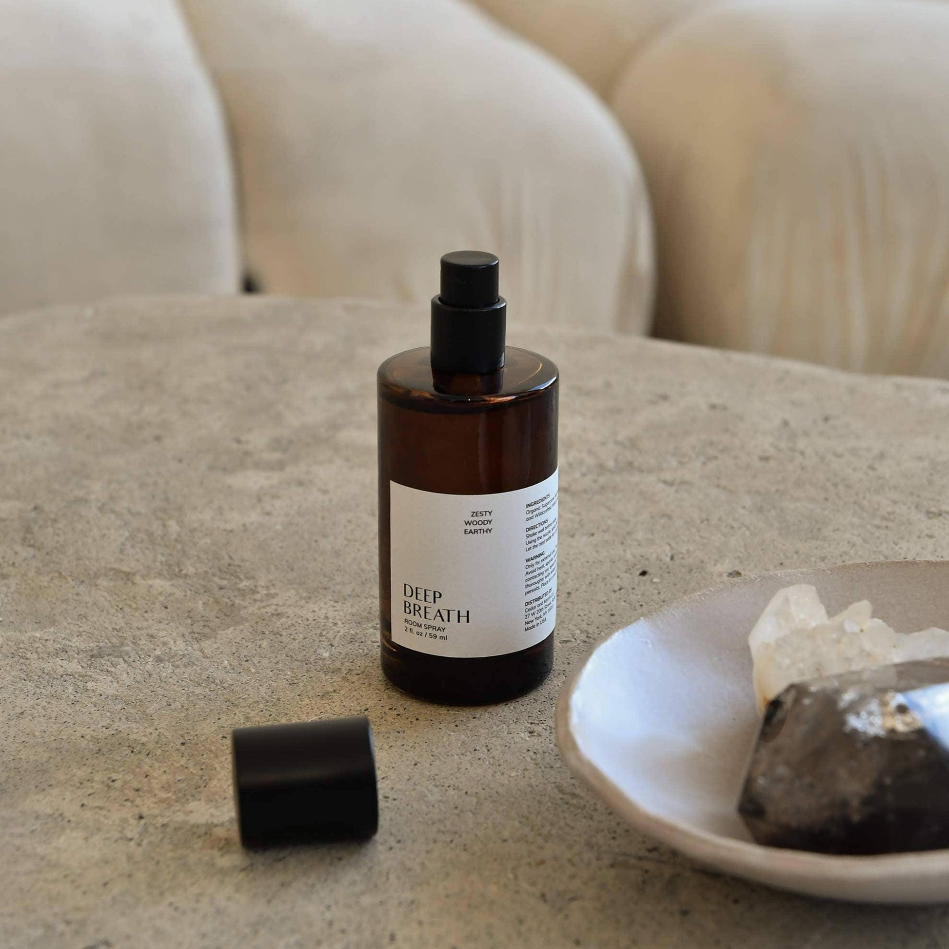 Amber glass bottle of Deep Breath room spray on stone table with decorative crystals in bowl. Come see us at Awaken, Franklin, Tennessee