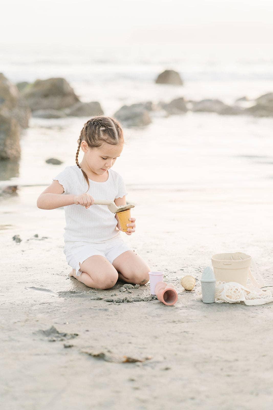 Young girl with braided hair playing with sand and buckets on a beach at sunset. Come see us at Awaken, Franklin, Tennessee