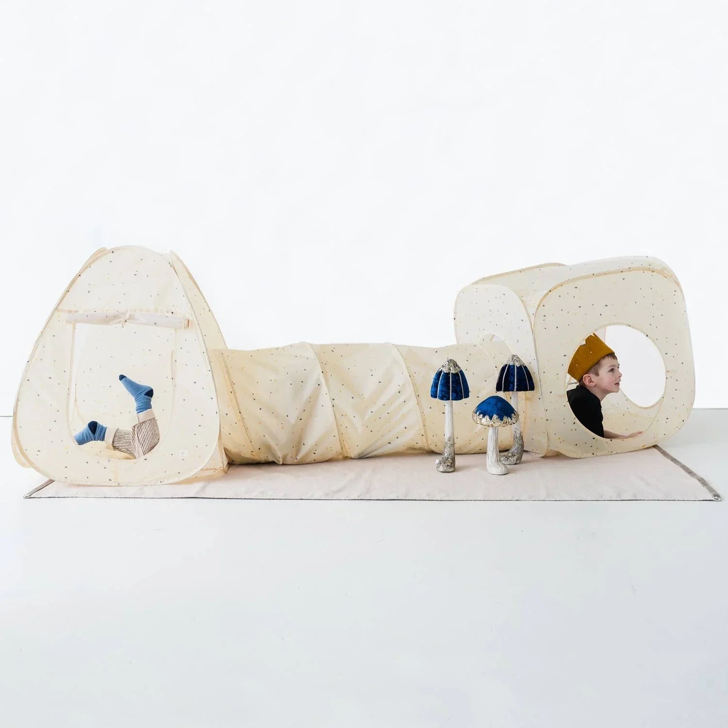 Children playing in beige fabric tunnel tent with blue mushroom toys on white floor. Come see us at Awaken, Franklin, Tennessee