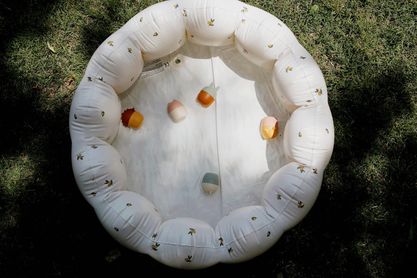 Inflatable white baby pool with yellow fruit pattern and colorful rattles on grass. Come see us at Awaken, Franklin, Tennessee
