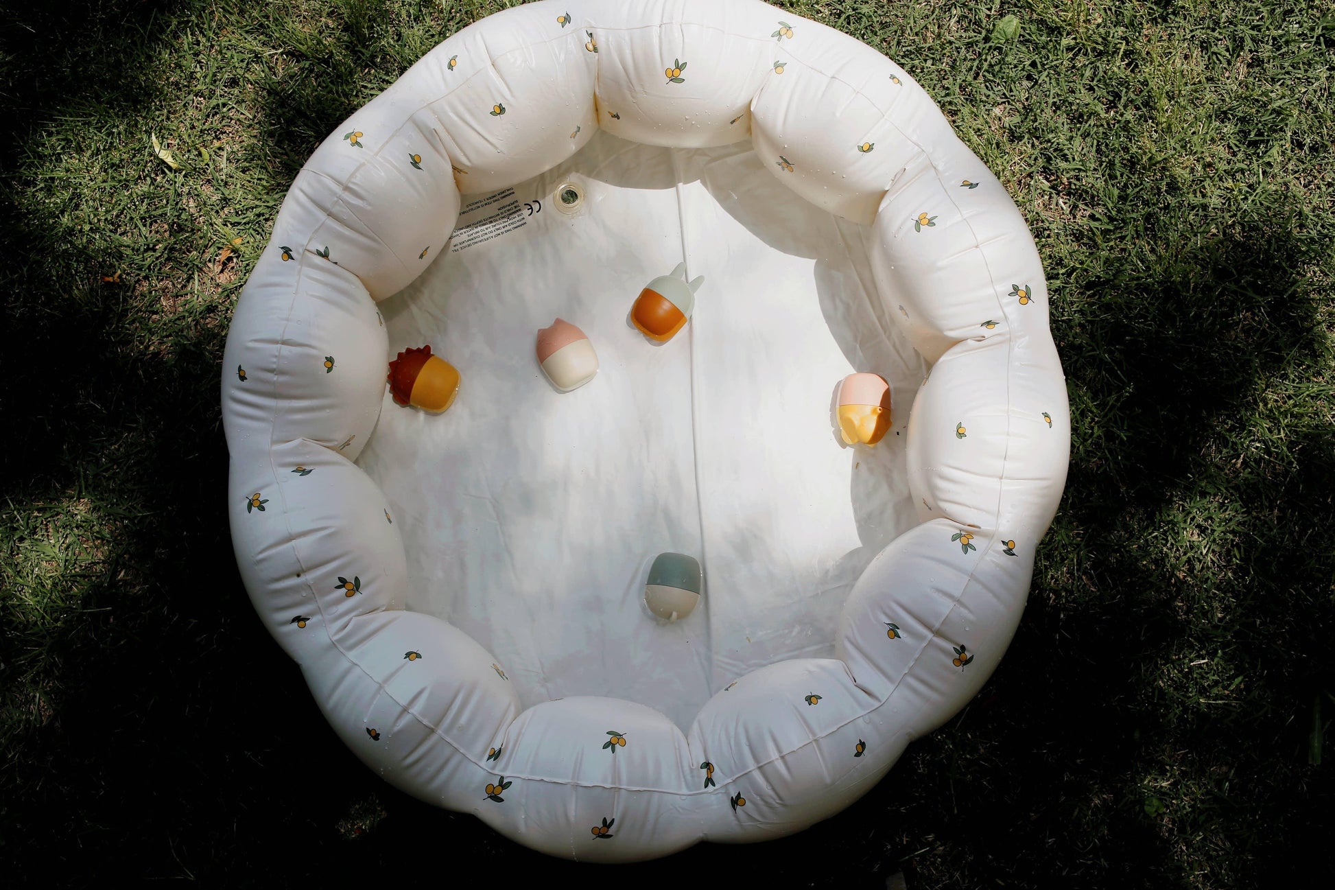 Inflatable white baby pool with yellow fruit pattern and colorful rattles on grass. Come see us at Awaken, Franklin, Tennessee